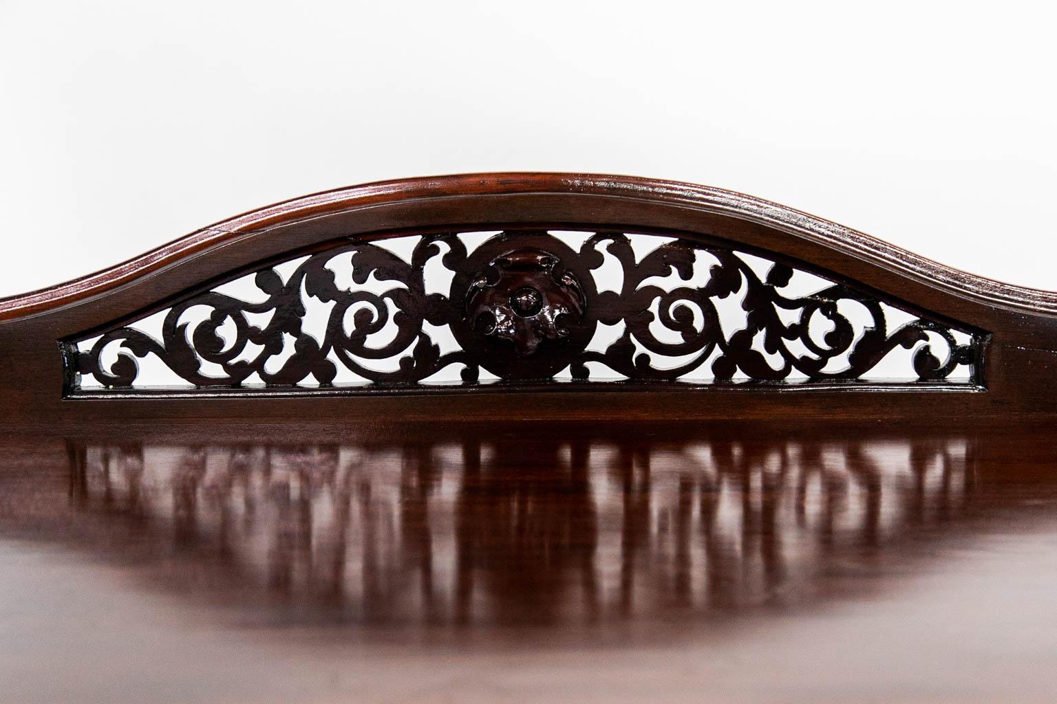 The top shelf of this server has a serpentine crest rail with an open pierced carved center. All three shelves in the crest rail have ogee molded edges. The lower two shelves have outward flaired galleries. The shelves are supported by tapered
