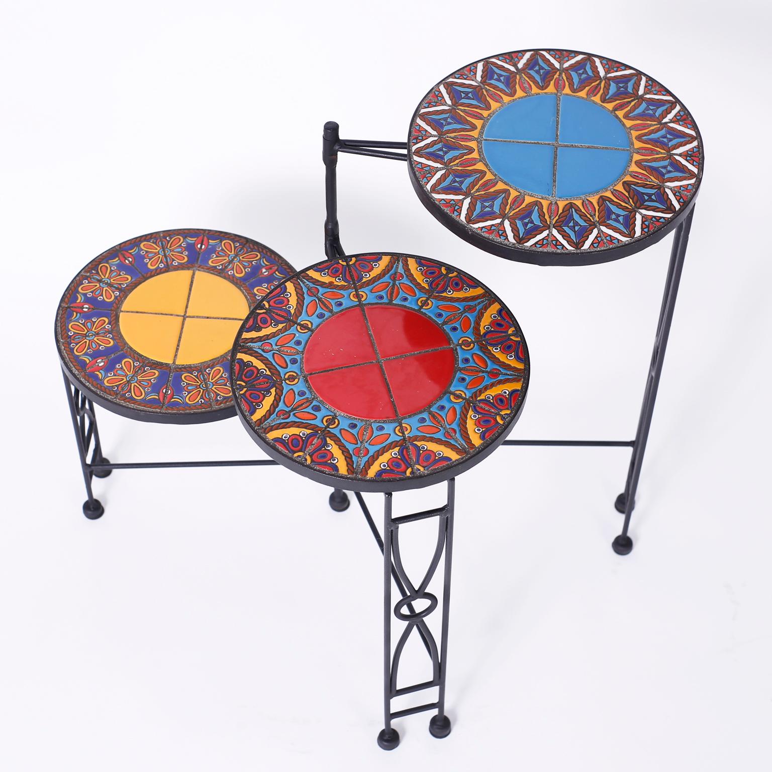 Midcentury adjustable three-tiered plant stand with an iron base and featuring bold colorful kaleidoscopic tile tops with floral and geometric designs.

Closed depth 12