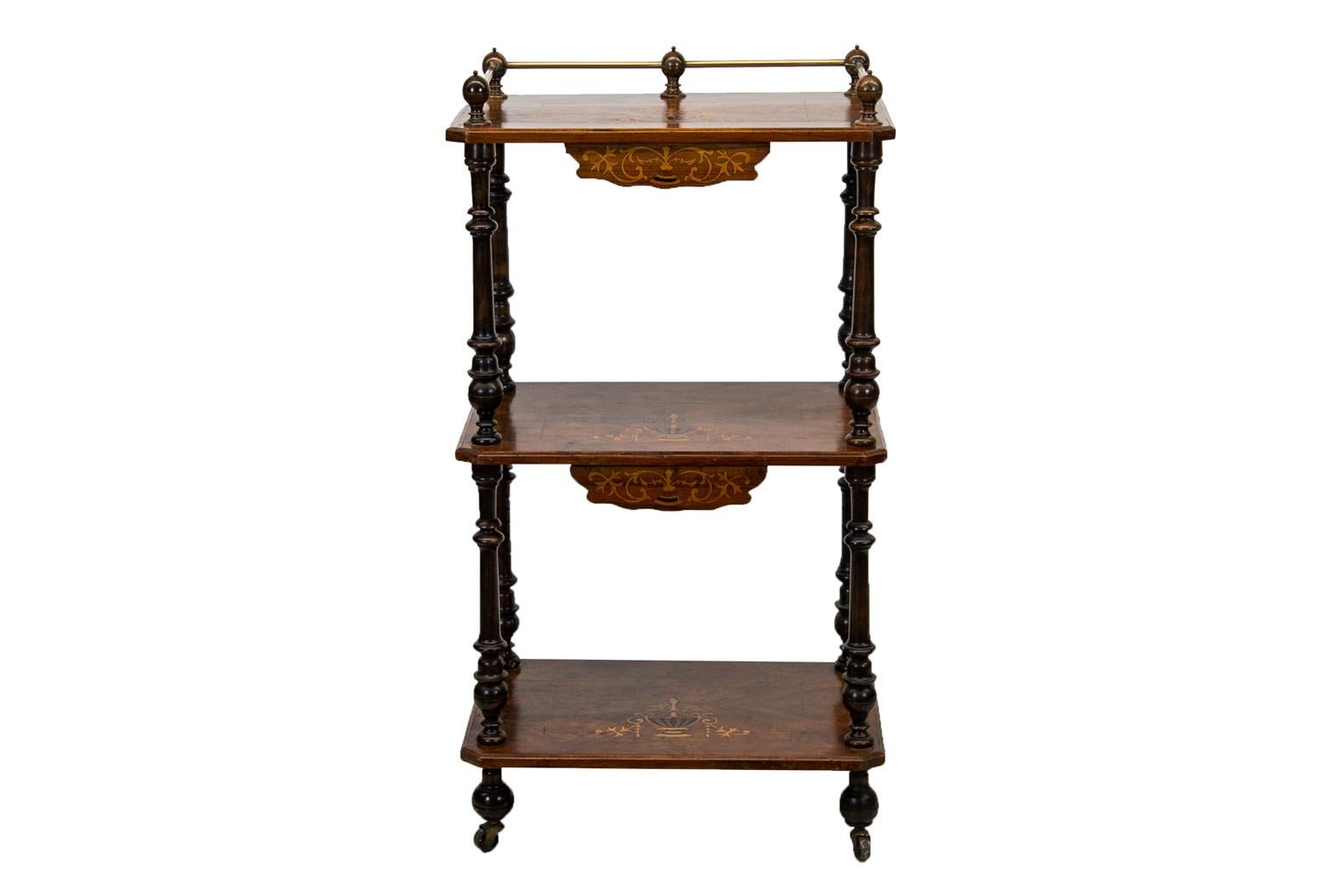 The three shelves of this shelf have bookmatched figured walnut. The edges are crossbanded with walnut and boxwood inlay. The top has a brass gallery supported by wooden finials. All three shelves have an inlaid classical urn that is composed of