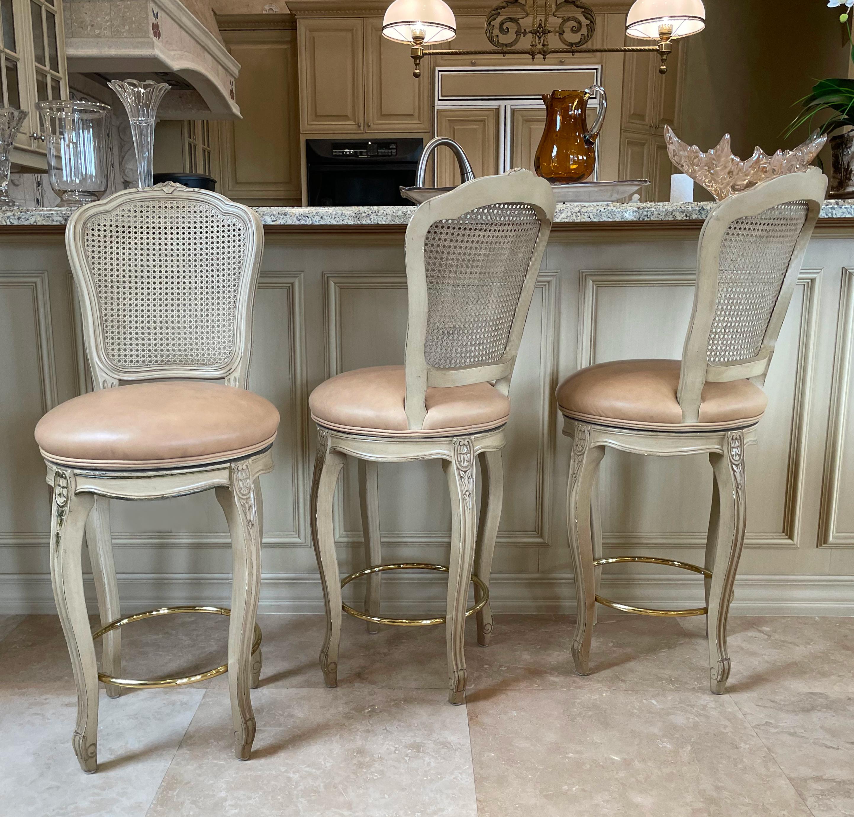 
Three Traditional Cane-Back Counter Chairs, Each in a Louis XV Style,
The cartouche-shaped back, leather-upholstered circular seats, on cabriole legs, joined by brass stretchers. 
Height back to floor 46 in. (116.84 cm.), Height seat to floor 29