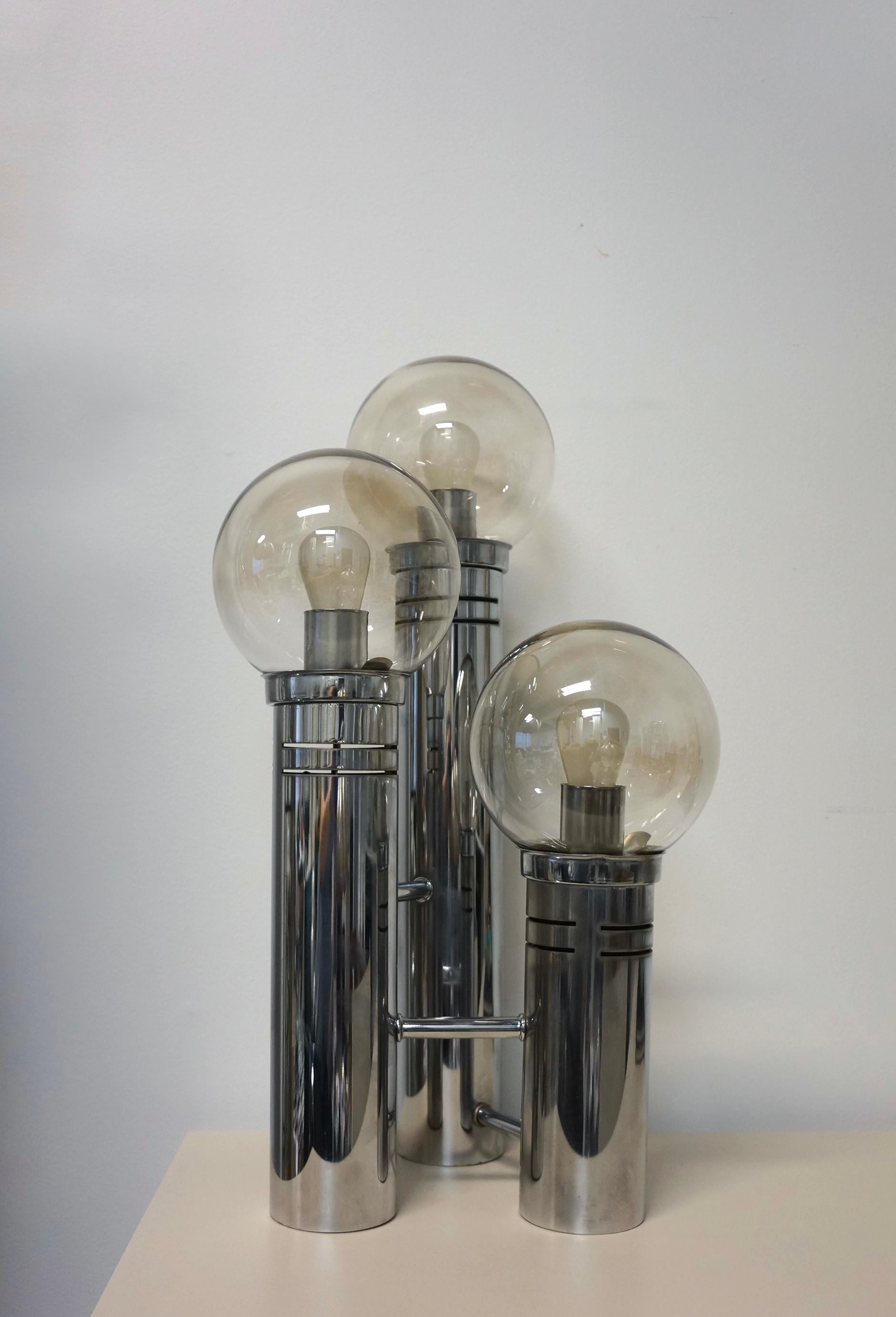 Stunning glass globe and chrome table lamp. This lovely lamp has three cylindrical tiers in varying heights that are connected at the chrome base featuring three glass globes. The slightly tinted glass globes cover the light bulbs. The glass globes