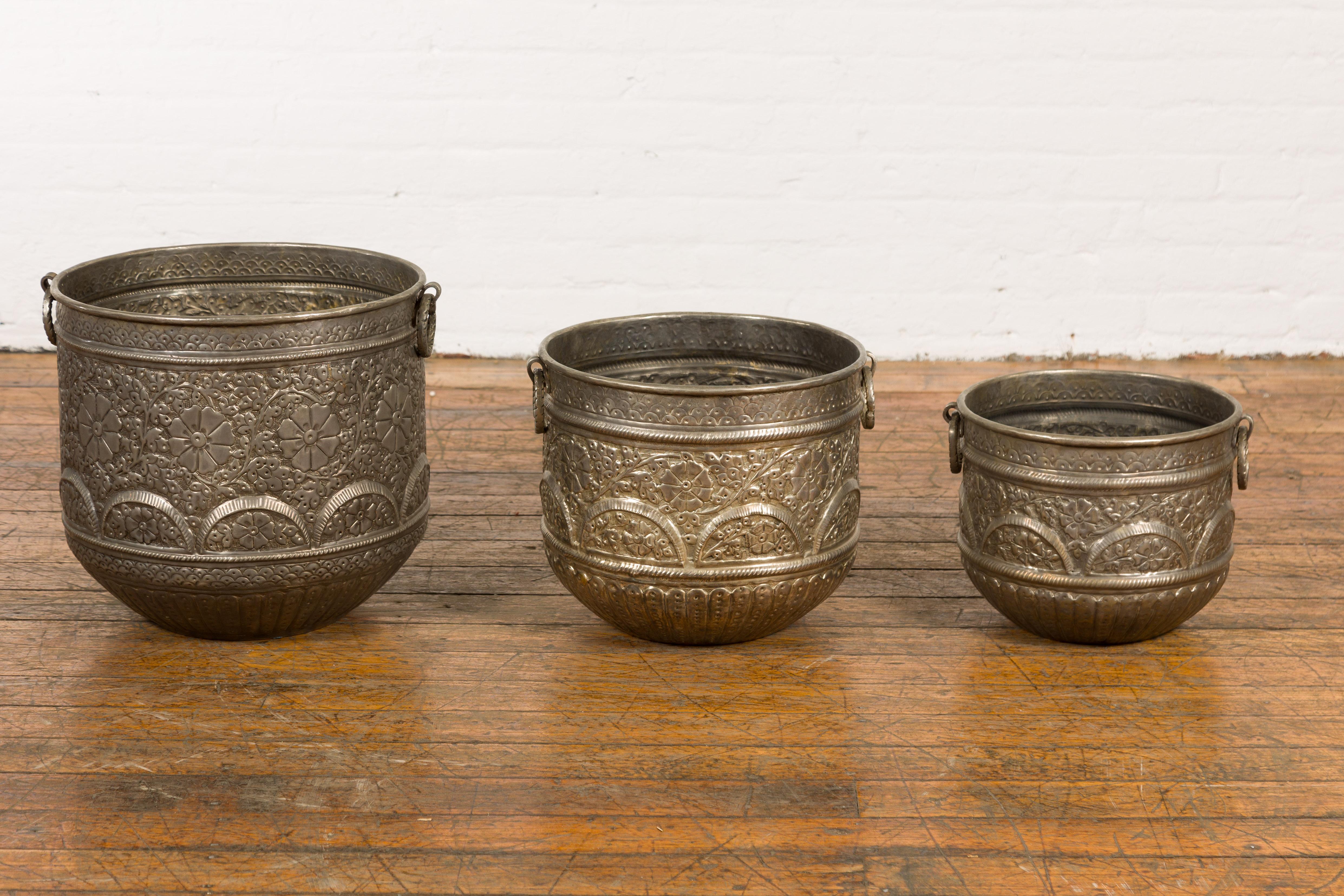 Set of three vintage Indian nested vessels made of silver over brass with abundant repoussé floral décor. Step into a world of traditional Indian craftsmanship with this set of three vintage nested vessels, expertly fashioned from silver over brass