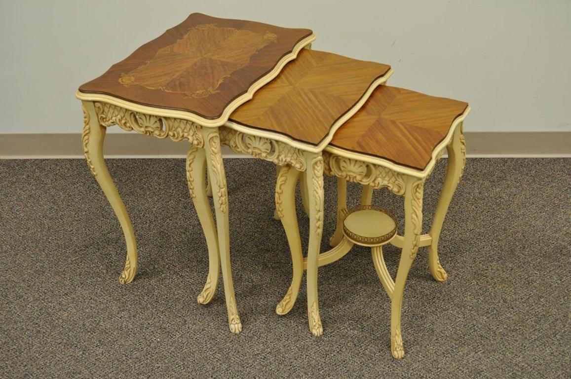 Set of three vintage French Louis XV style carved, painted, and satinwood inlaid nesting side tables. Item features beautifully carved bases, satinwood inlaid tops, and elegant overall form, circa mid-1900s. Measurements: 25