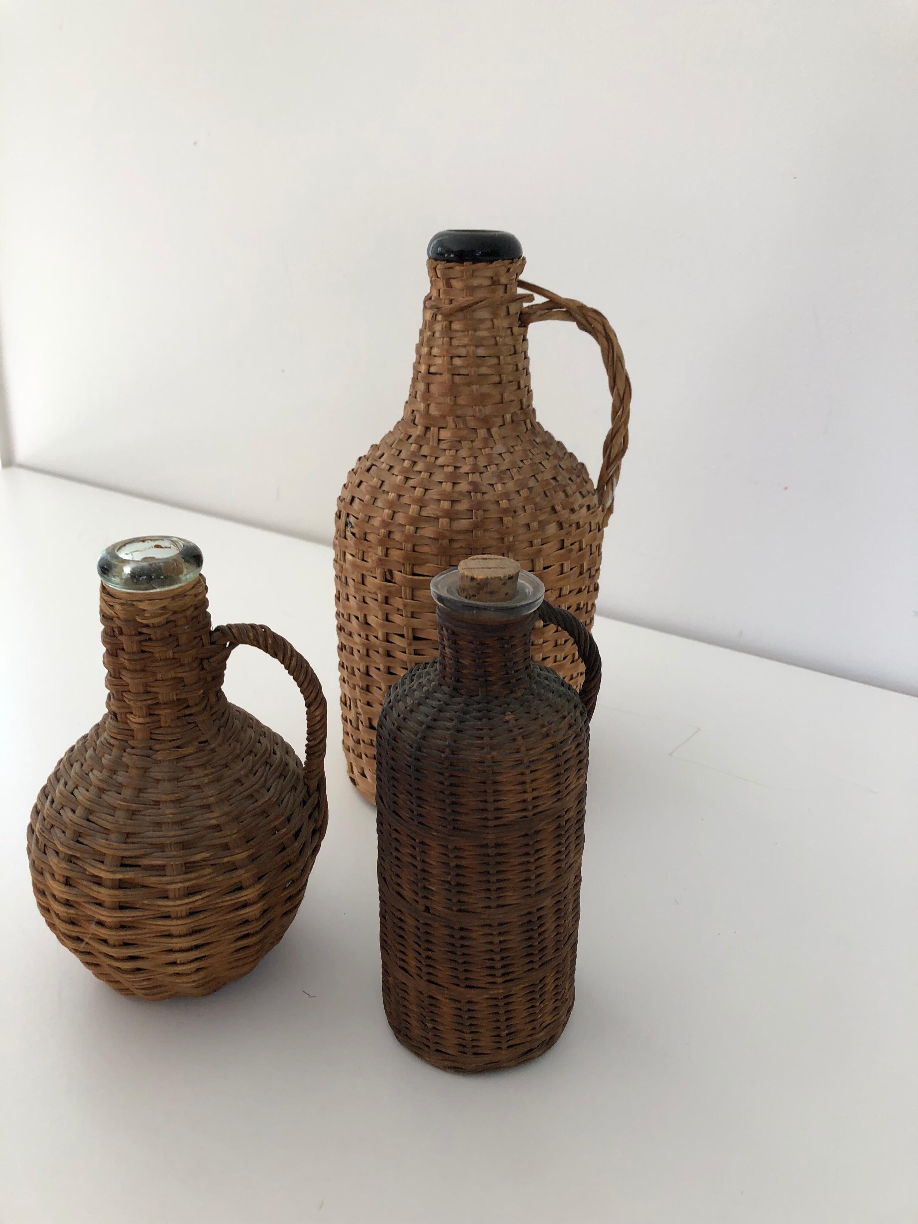 An assembled collection of three vintage wicker wrapped glass liquor or wine jugs. Small jug measures 5.5