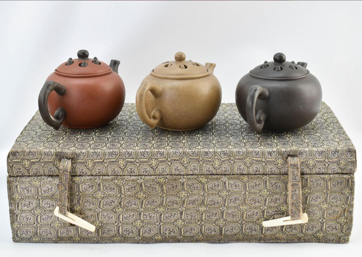 Three yixing teapots in a velvet lined box. Each teapot is a different color clay: red, purple, and yellow. With moveable pieces in the lids. Impressed/marked on the underside, though each bears a different character mark.
