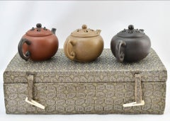 Three yixing teapots in a velvet lined box. Each teapot is a different color.