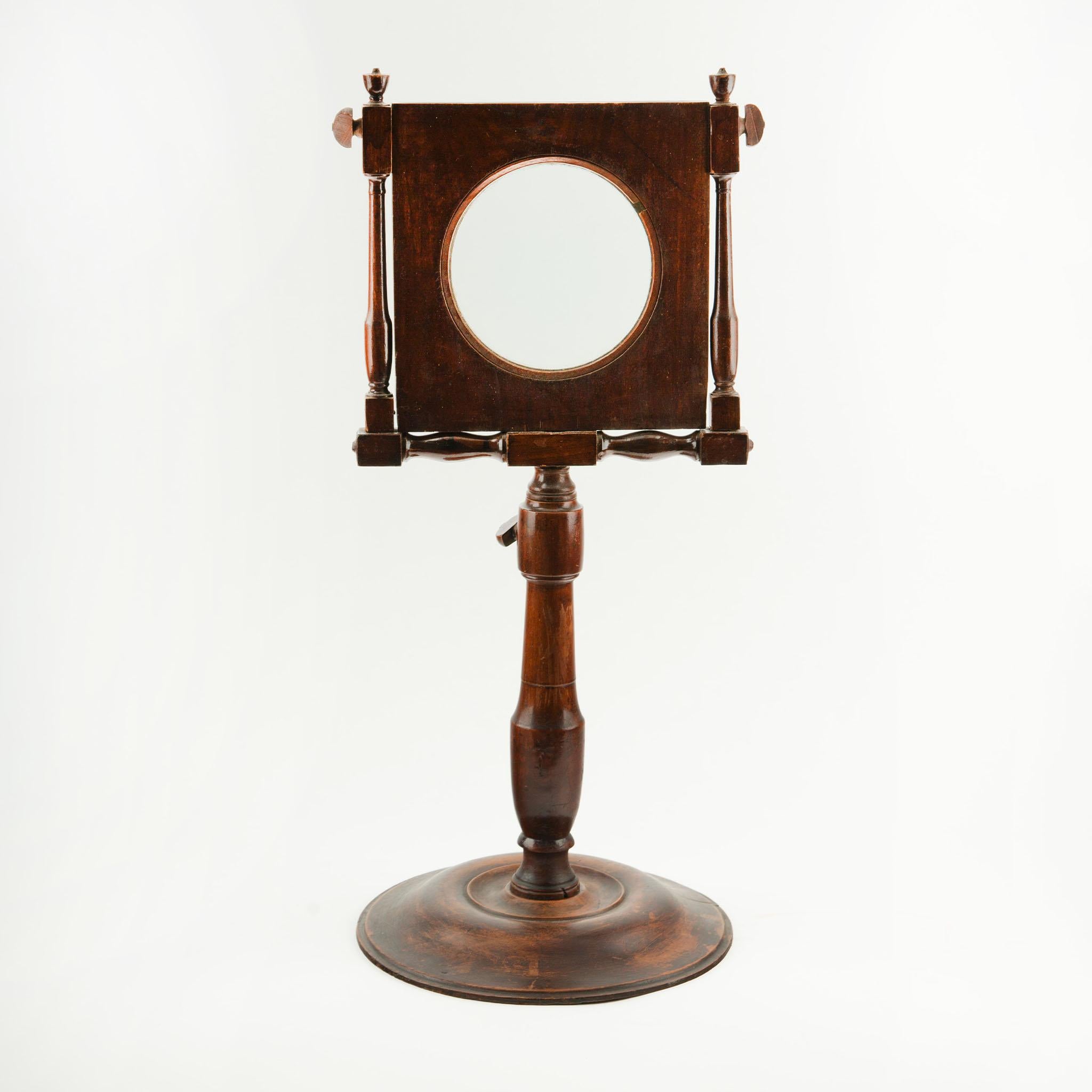 A beautifully crafted 19th-century standing magnifying glass, featuring a circular lens mounted within an elegant, square wooden frame. The frame is supported by four turned spindles and is adjustable in angle, allowing for precise positioning. This