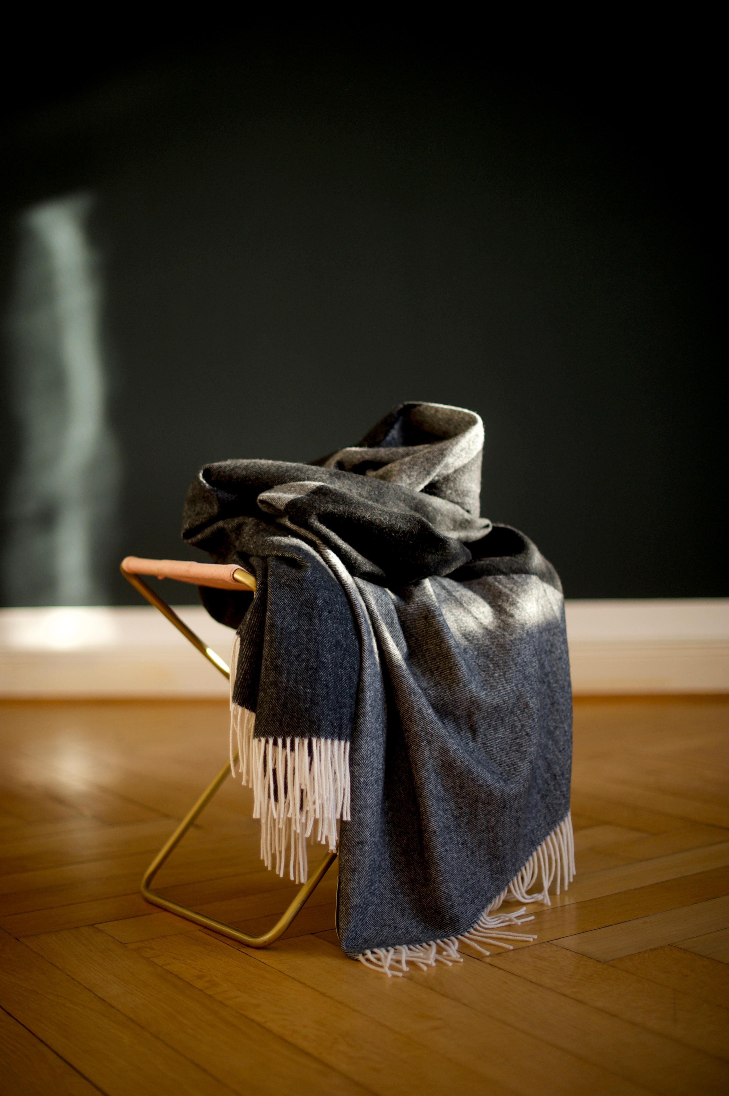 Diseñada en Berlín por Catharina Mende, tejida con 90% de merino y 10% de cachemira en Escocia: Esta exquisita manta en diferentes grises es la compañera perfecta, favorecedora y cálida, para cada estación y una pieza de lujo y belleza para cada