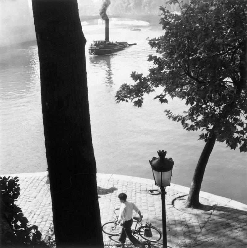 "Paesaggio della Senna" di Thurston Hopkins

16 agosto 1952: Un uomo passeggia in bicicletta lungo la Senna a Parigi e un rimorchiatore sul fiume emette fumo dal suo fumaiolo. Pubblicazione originale: Picture Post - 6002 - Paris Pride - pub.