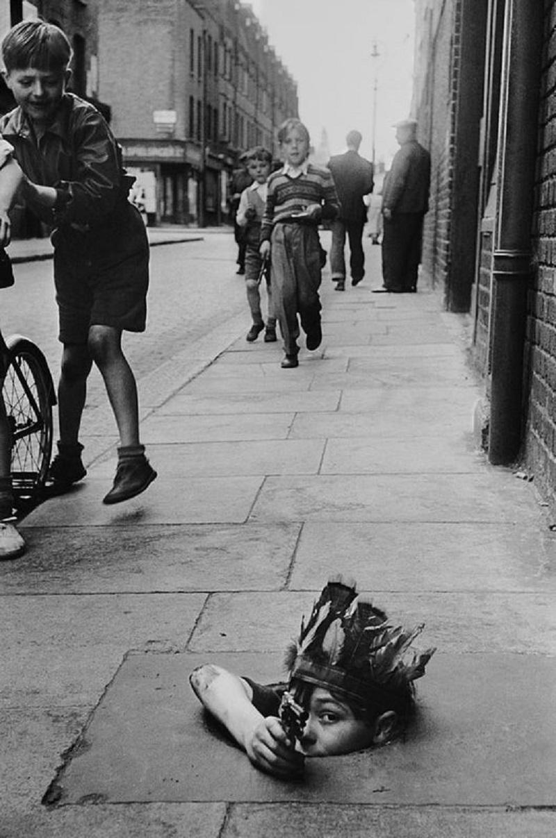 "Street Games" by Thurston Hopkins

A young child wearing an Indian headdress hides in a coal hole as he takes aim under the watchful eye of a friend. Original Publication: Picture Post - 7230 - Children Of The Streets - pub. 1954

Unframed
Paper