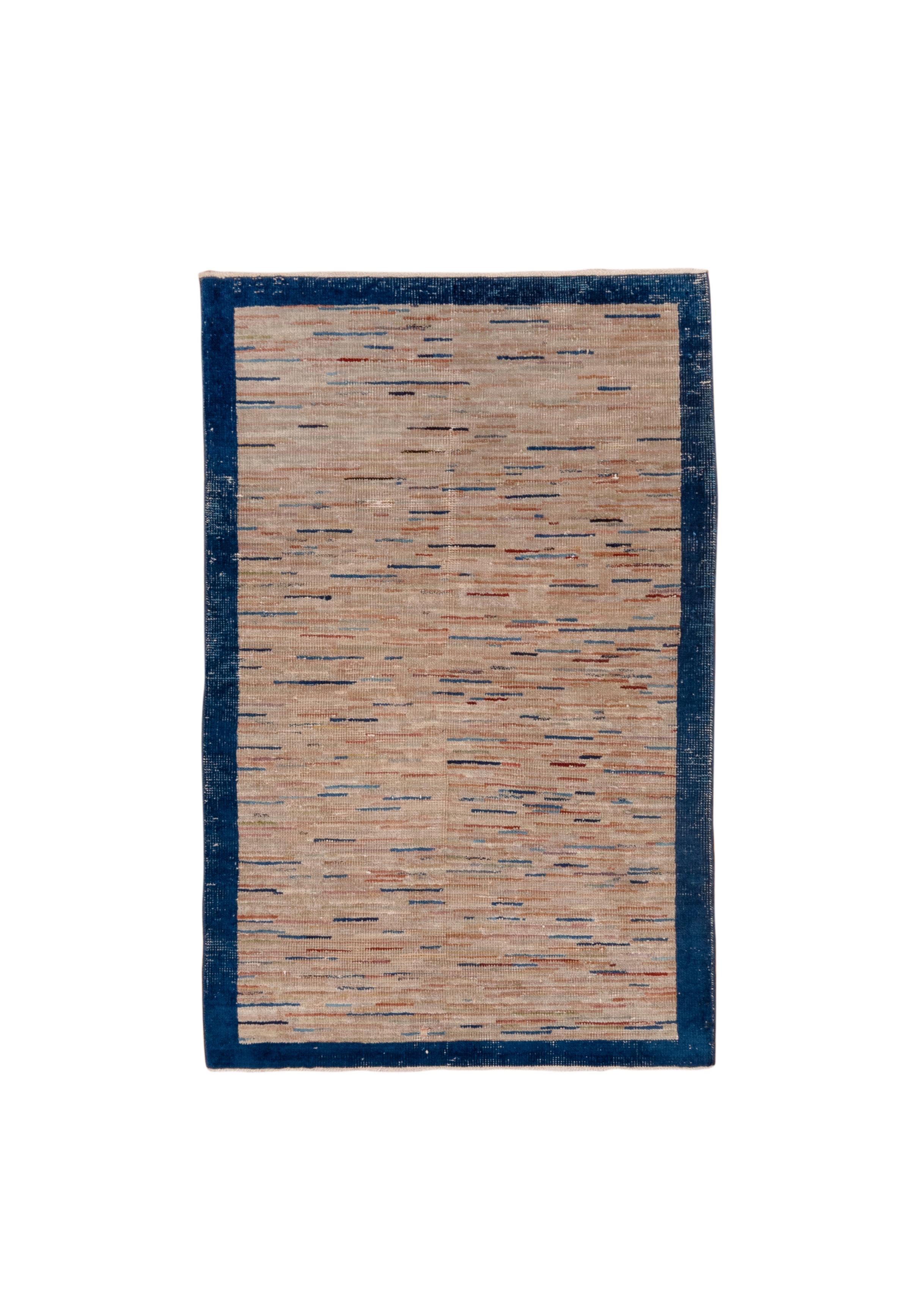 This is an “end of day” rug incorporating the yarn bits left over from weaving larger carpets.  The field is generally putty-toned, with lines in various blues and reds. Plain navy border. Wear ribbing to pile, but quite floorable withal. 

Rug