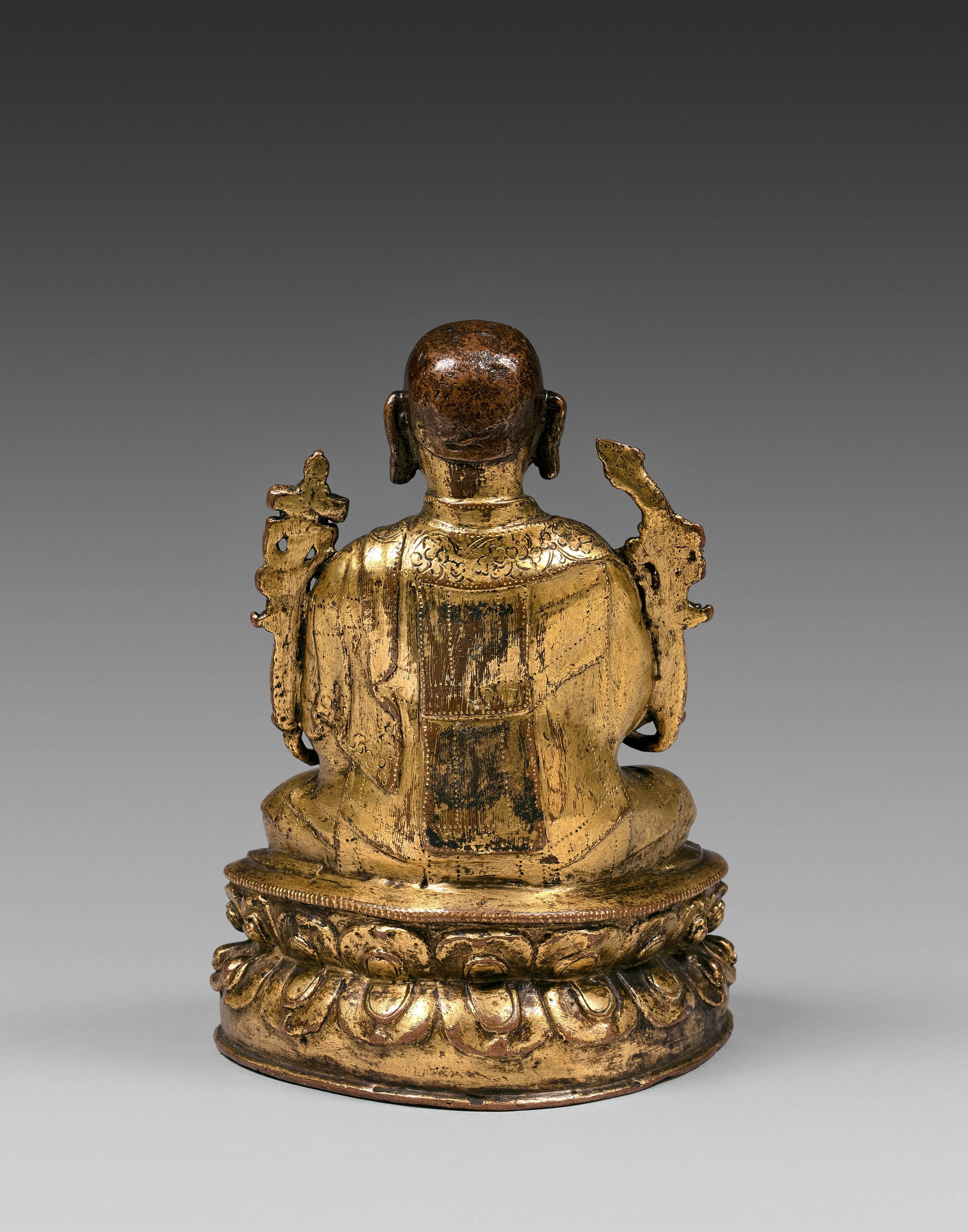 The lama seated in vajrasana on a lotus pedestal, the hands in teaching mudra and holding two lotus flowers blossoming on the shoulders, dressed in a monastic robe with floral scrolls delicately chiseled, the base unsealed.

Provenance : Italian