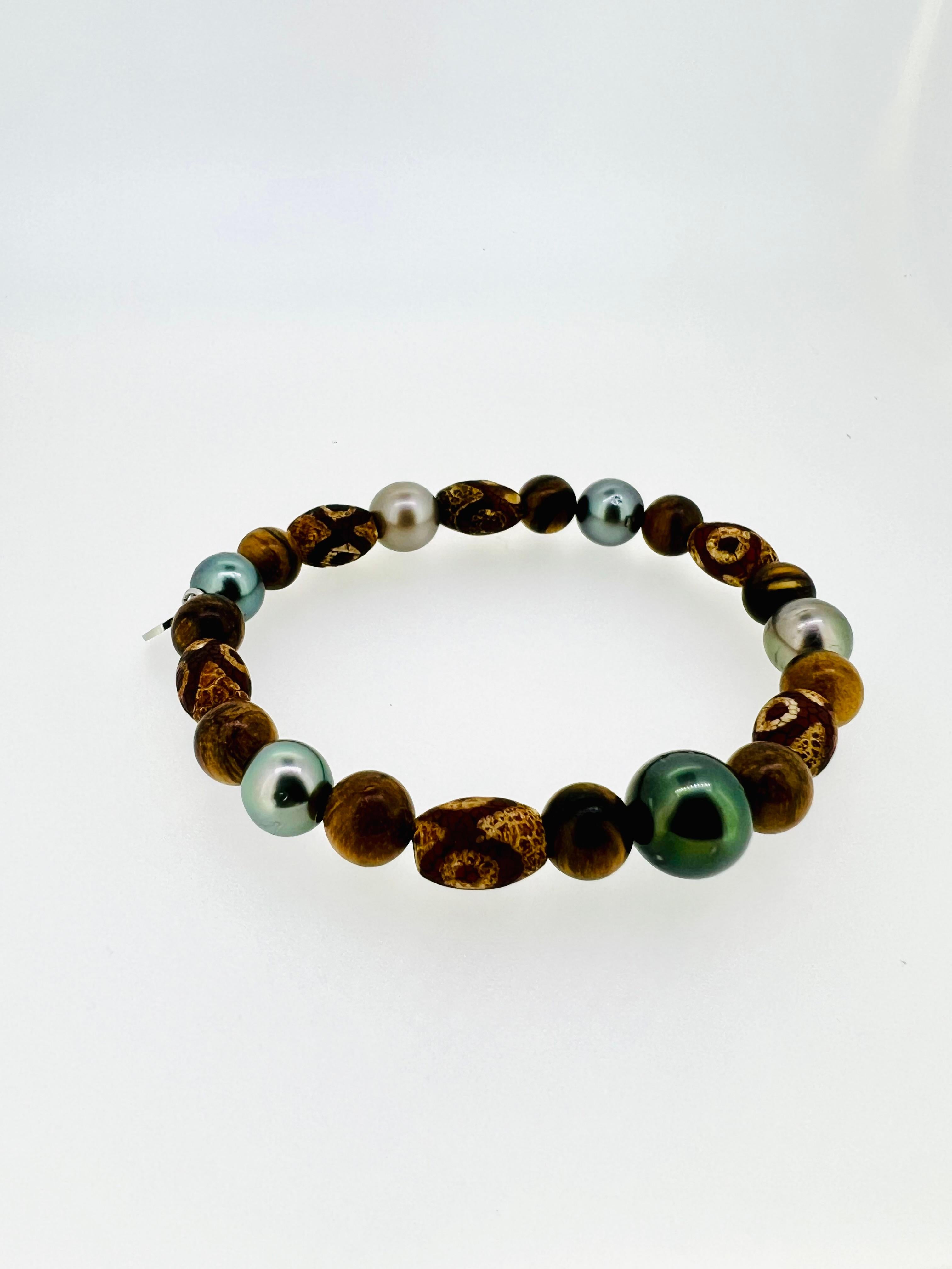 Introducing a distinctive men’s bracelet crafted from Tibetan agate in barrel-shaped beads (1cm), paired with 8mm Tiger Skin wood and 9-12mm Tahitian pearls in varying shades of gray. This unique combination of natural tones exudes a refined yet