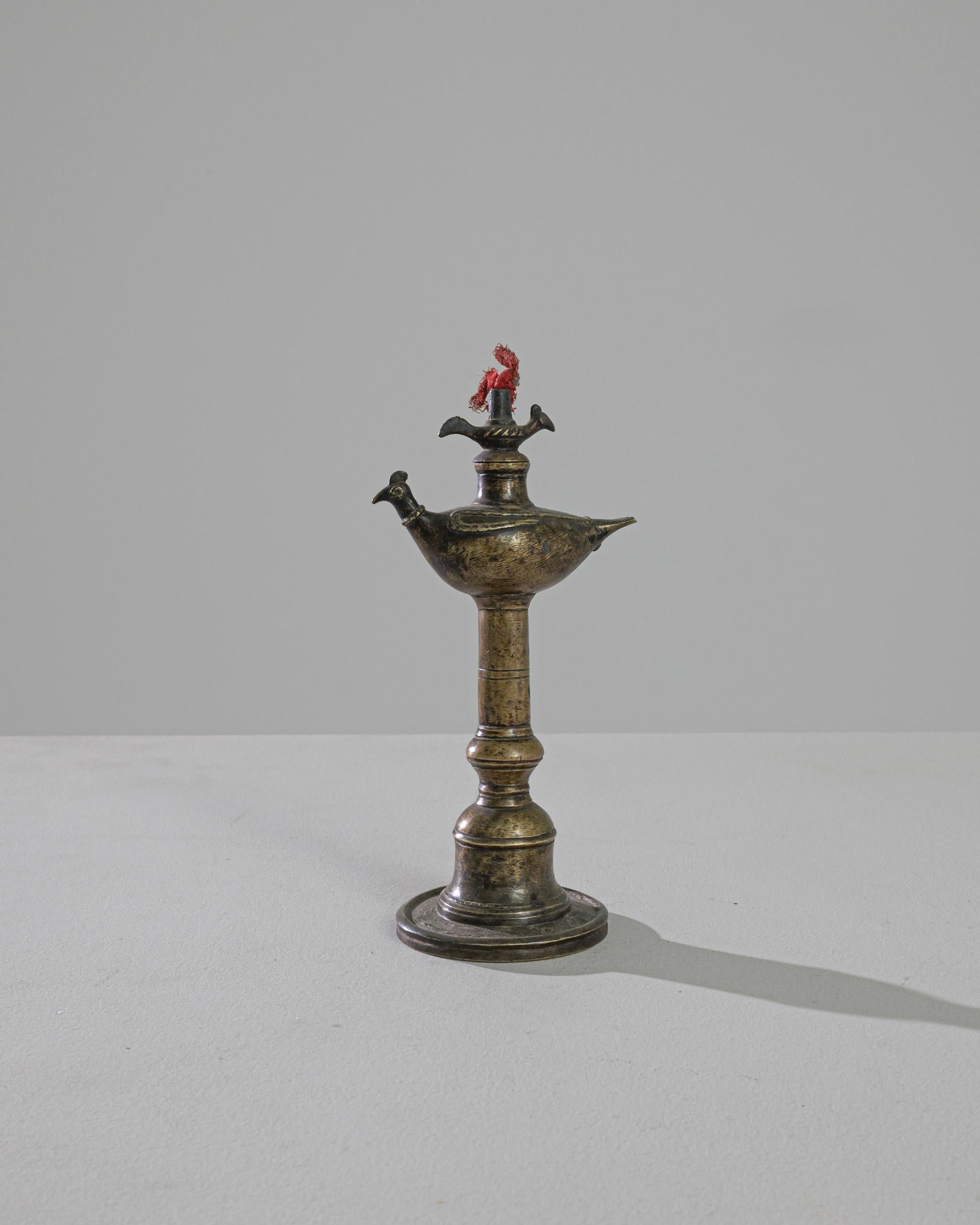A brass oil lamp from Tibet, this piece displays a little elephant on top of an ornamented column resembling a bell. With a miniature friend flying above, this expectant fowl is poised for the fire to start. The authentic patina exhibits golden