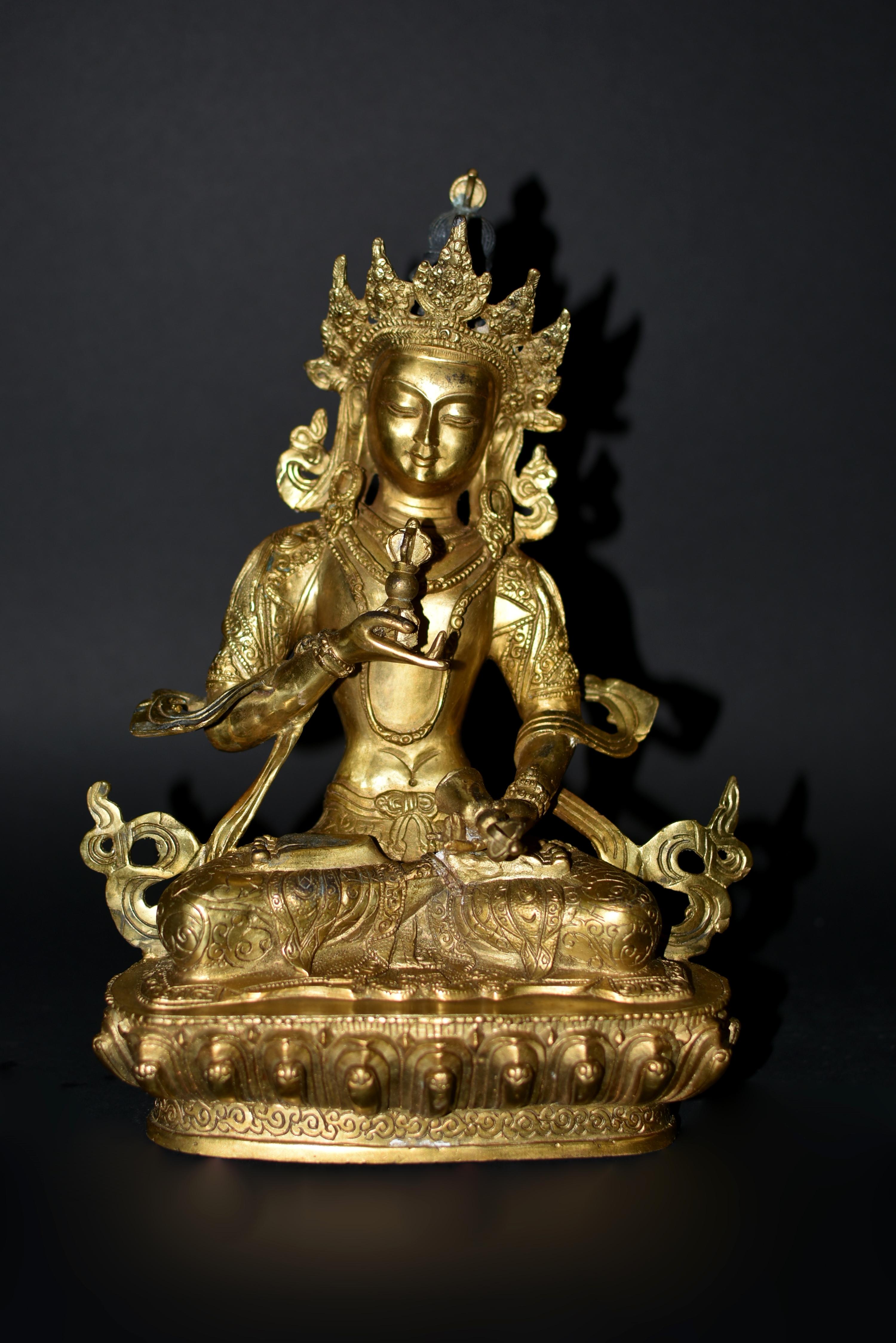 A beautiful gilt bronze Tibetan Vajrasattva statue. The serene face with large downcast eyes under arched eyebrows above pursed lips, flanked by long earlobes, under hair tied in double buns and adorned with an elaborate crown. Clad in a embroidered
