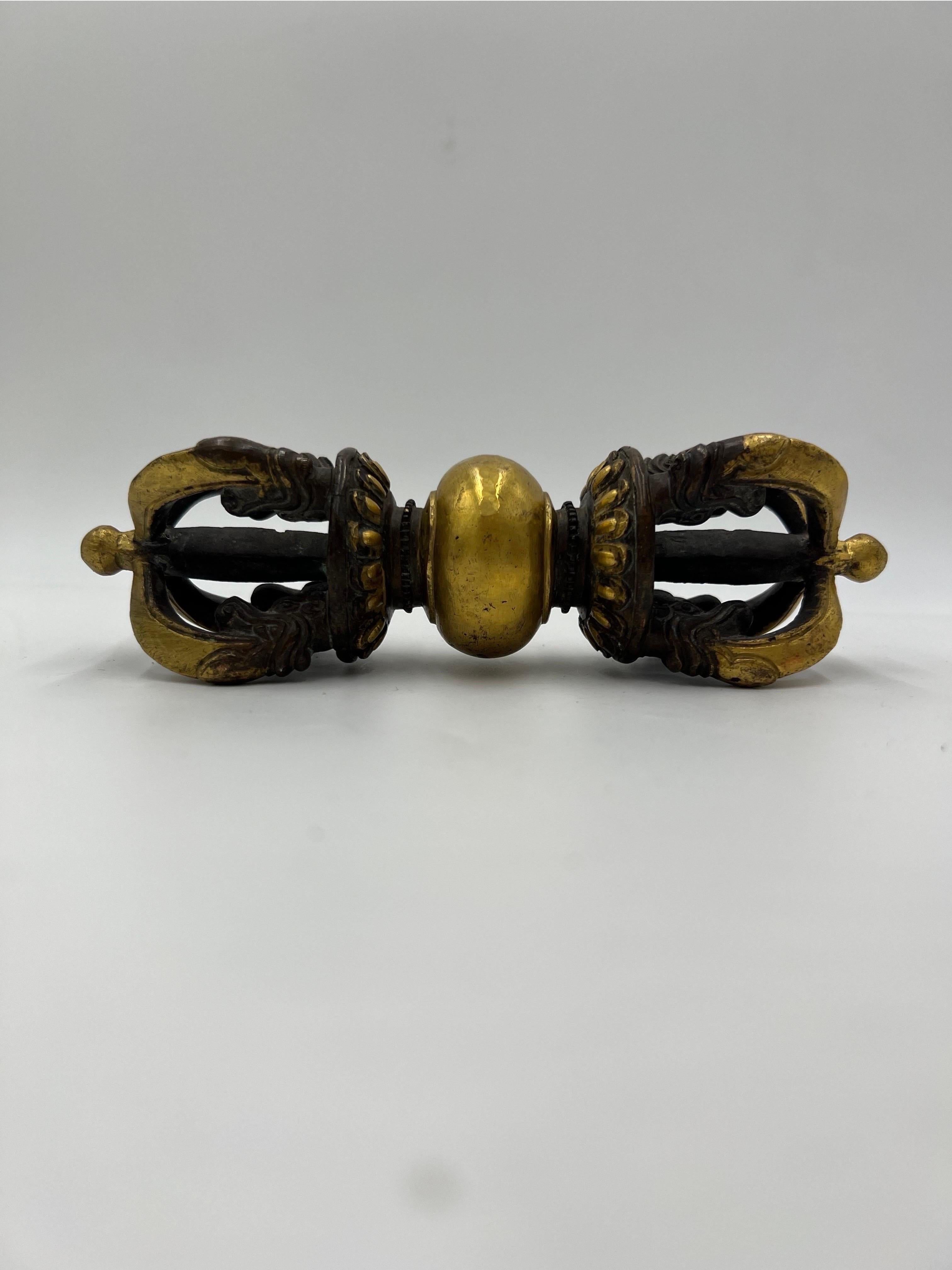 A Tibetan Buddhist gilded cast bronze Vajra The gilt bronze Vajra thunderbolt-scepter is cast with a central bulbous grip that separates two lotus pedestals supporting a central column surrounded by four arched vajra points emerging from the jaws of