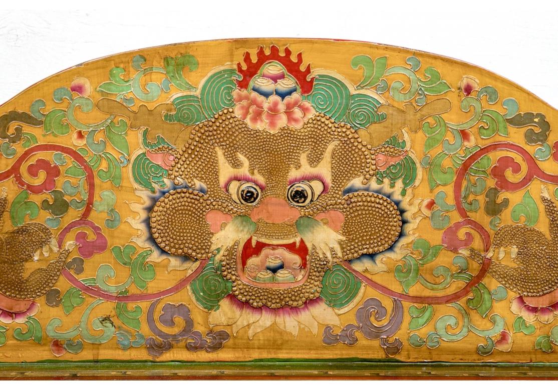 A long carved wood bench with shaped top and seat rail and raised shaped sides with finials. The whole brightly painted with overall decoration featuring tigers and confronting dragons on the seat. Dragon masks appear on the back and the four lower