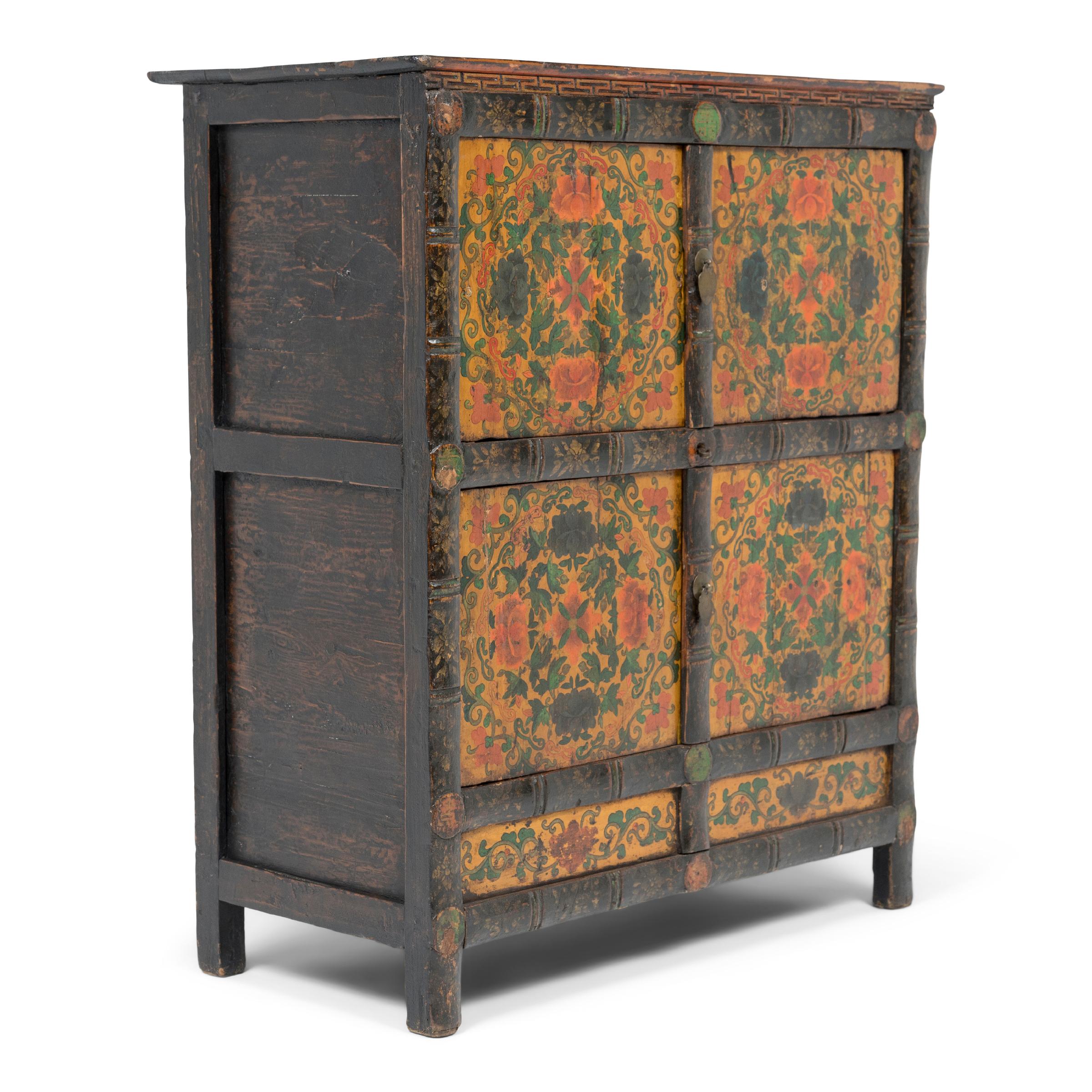 This 19th-century storage cabinet is intricately hand-painted in the Sino-Tibetan style with brightly pigmented gouache paints in a palette of yellow, orange, green, and black. The cabinet front is divided into six inset panels, each painted with