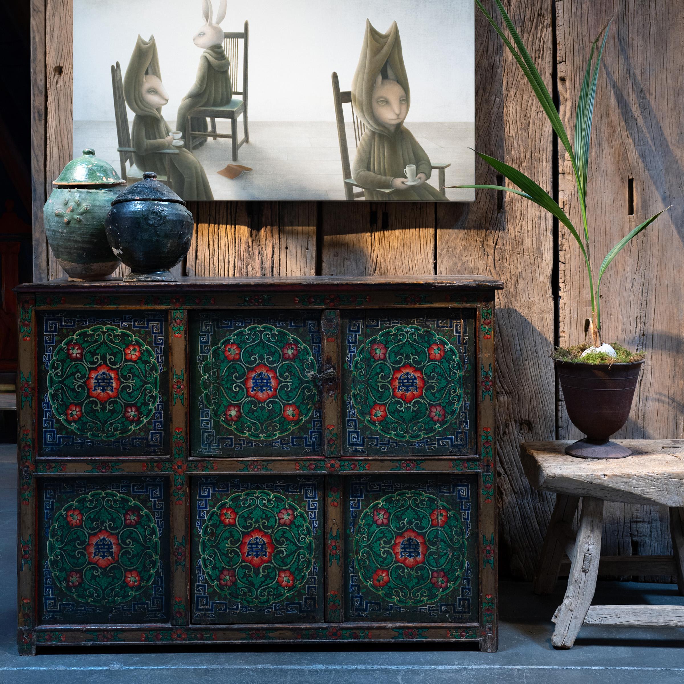Crafted in 19th-century Tibet, this extraordinary cabinet is beautifully decorated from end to end with hand-painted floral motifs. Brushed in a cool palette of green, red, blue and gold, the painted facade is a celebration of traditional artistry