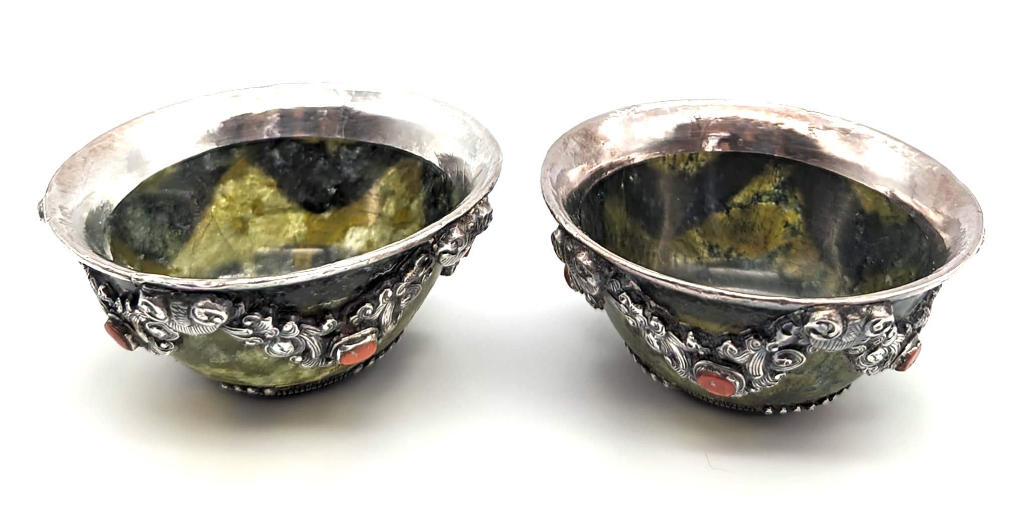 Offered is a pair of handcrafted sculpted and hammered jade Tibetan tea cups embellished with embossed sterling silver motifs and red coral cut stones inset. The jade is dark, yet semi-transparent and light passes through. Can be used as salt bowls,