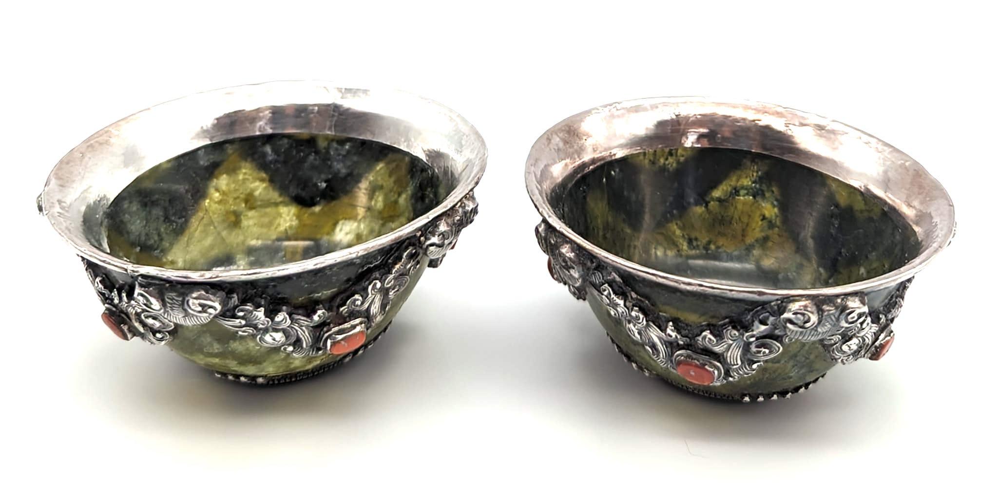 In offerta c'è una coppia di tazze da tè tibetane in giada scolpita e martellata a mano, impreziosite da motivi in rilievo in argento sterling e pietre di corallo rosso incastonate. La giada è scura, ma semitrasparente e la luce passa attraverso di