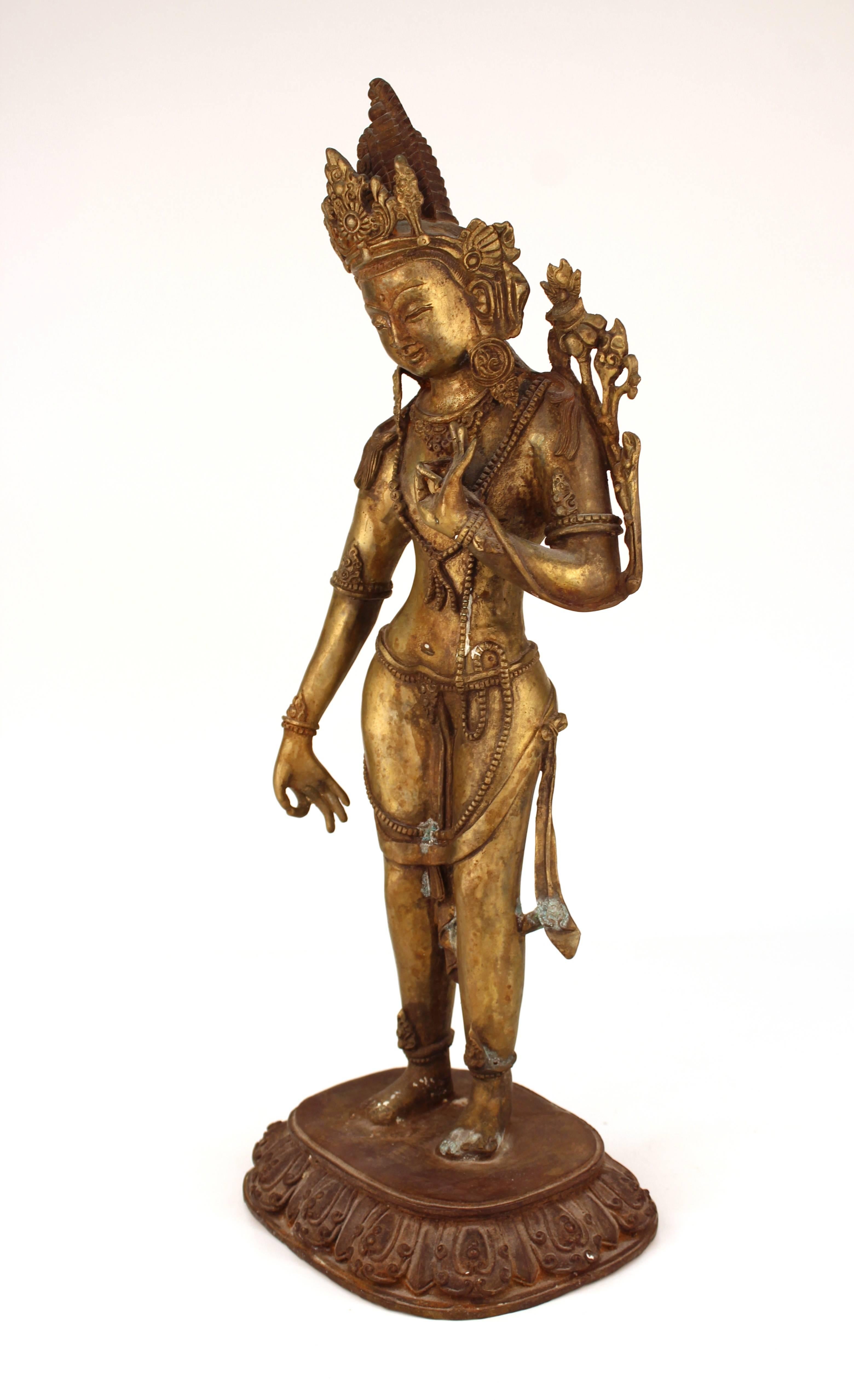 Tibetan or Indian Hindu gilt brass figure of a standing Bhumi Devi on a throne, her proper left hand holding Utmala, the night lotus, her right hand in abhaya mudra. The piece has some areas of green encrustation to the patina.