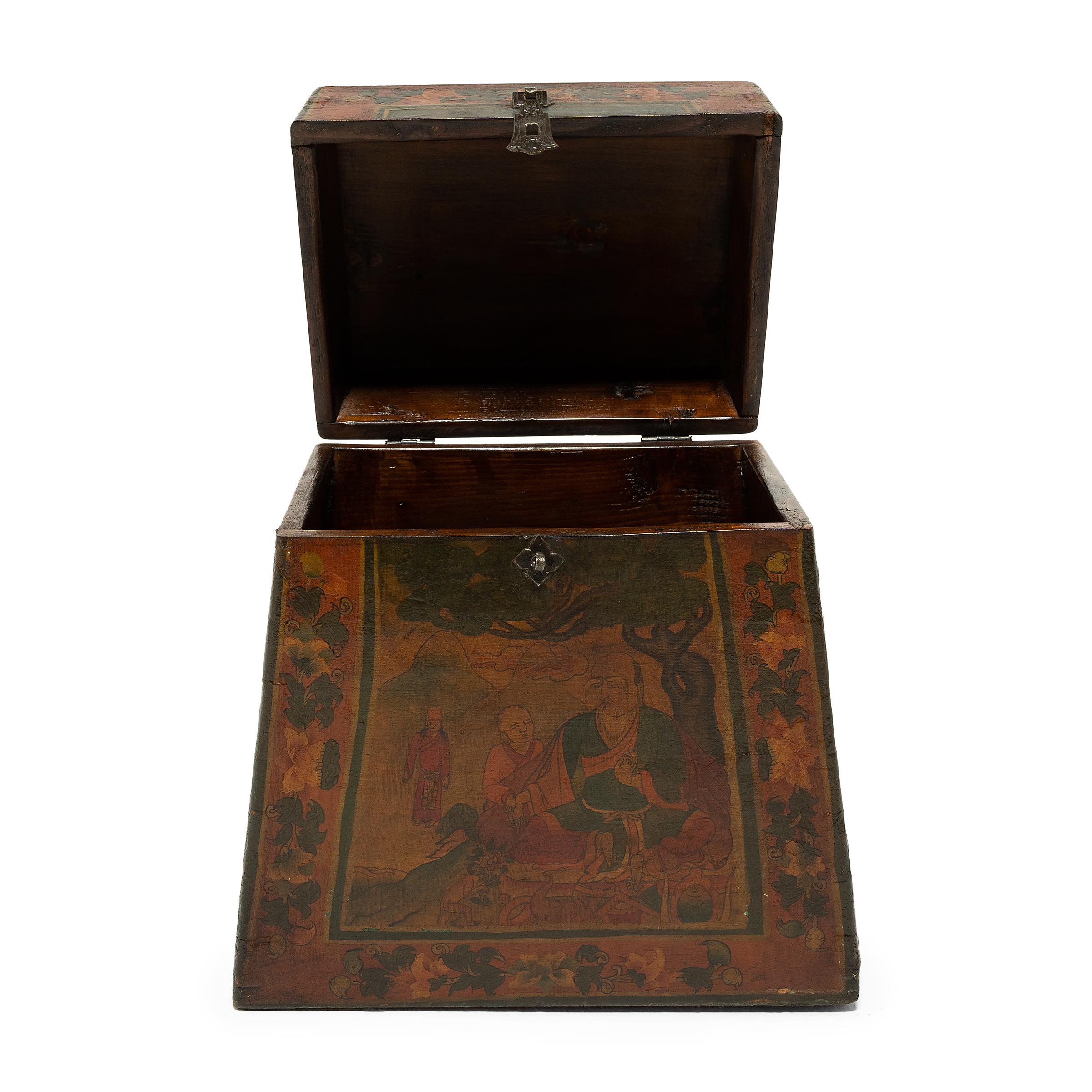 This beautiful late 19th-century Tibetan box has an unusual trapezoidal form and is highly decorated in the Sino-Tibetan style in a palette of red, orange, yellow and green. The scene painted on the front of the box is a variation of a traditional