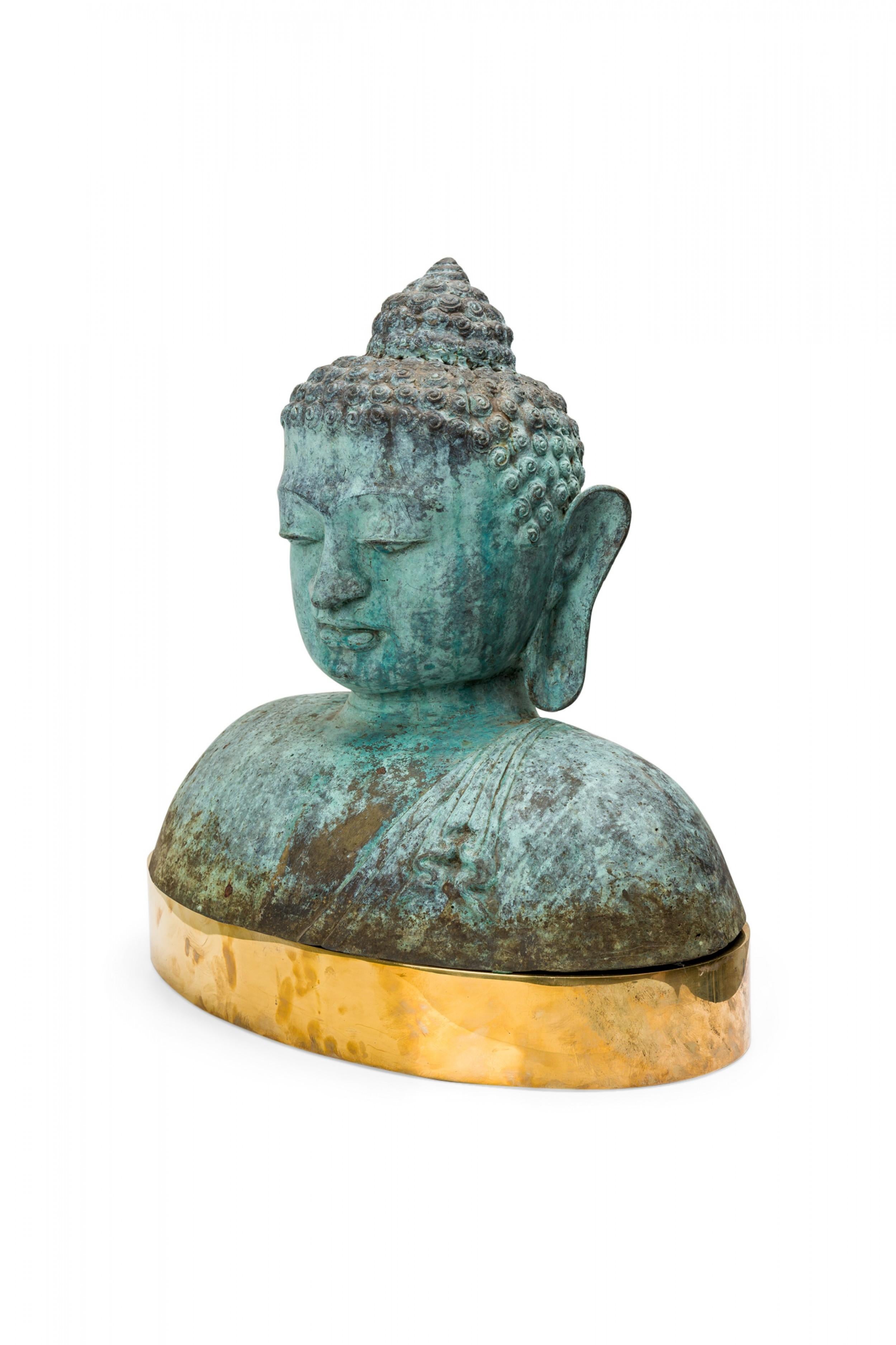 Vintage Tibetan bronze figural bust of the Buddha with a natural green patina, resting on an oval polished brass plinth.