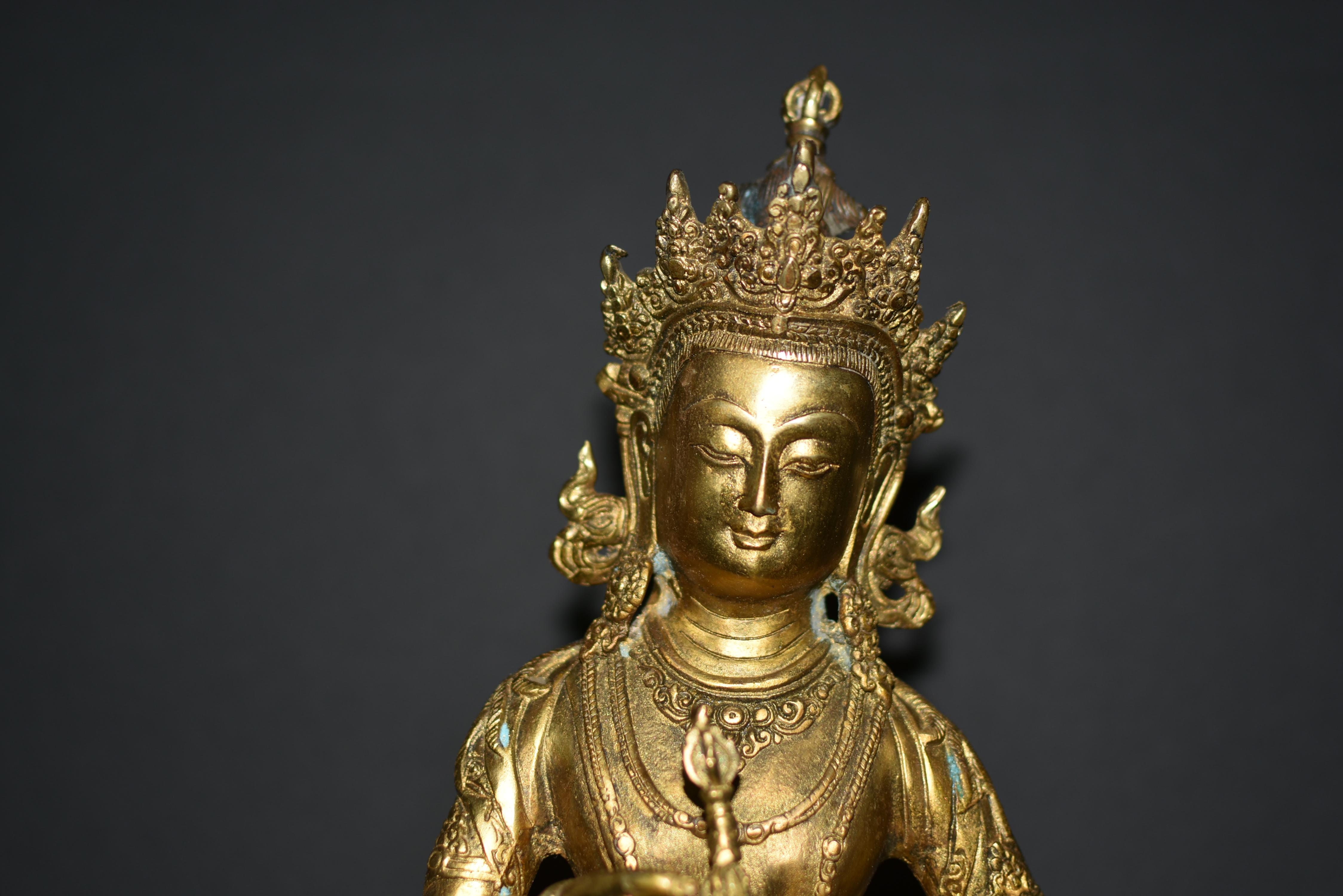 This gilt bronze sculpture of Buddha Vajrasattva stands as a testament to the sublime craftsmanship and spiritual significance of Tibetan Buddhist art. Weighing a substantial 7.25 pounds, the sculpture portrays the enlightened deity seated in the