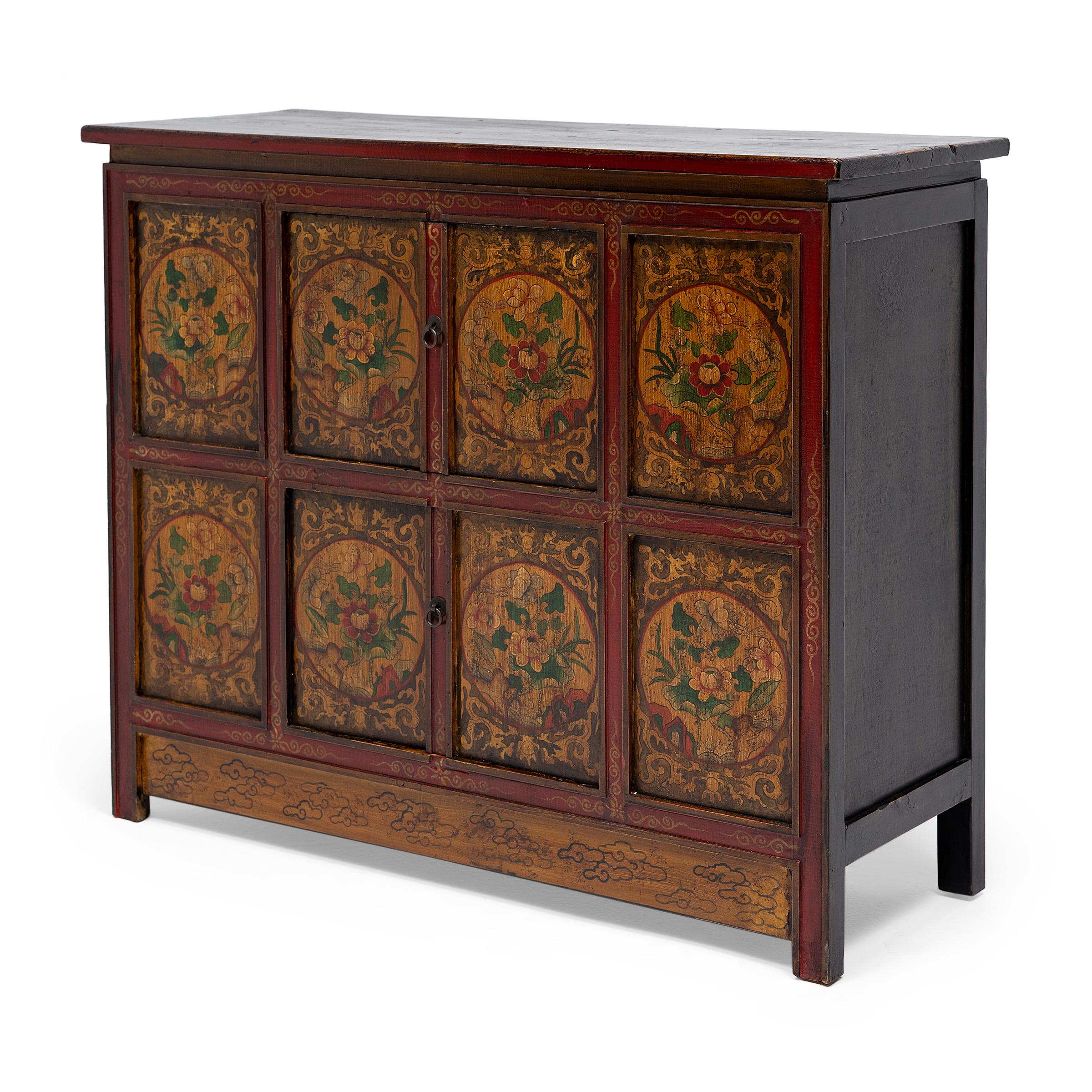 This late-19th century storage cabinet is intricately hand-painted in the Sino-Tibetan style with brightly pigmented gouache paints in a palette of red, yellow, green, and black. The cabinet front is divided into eight inset panels, each painted