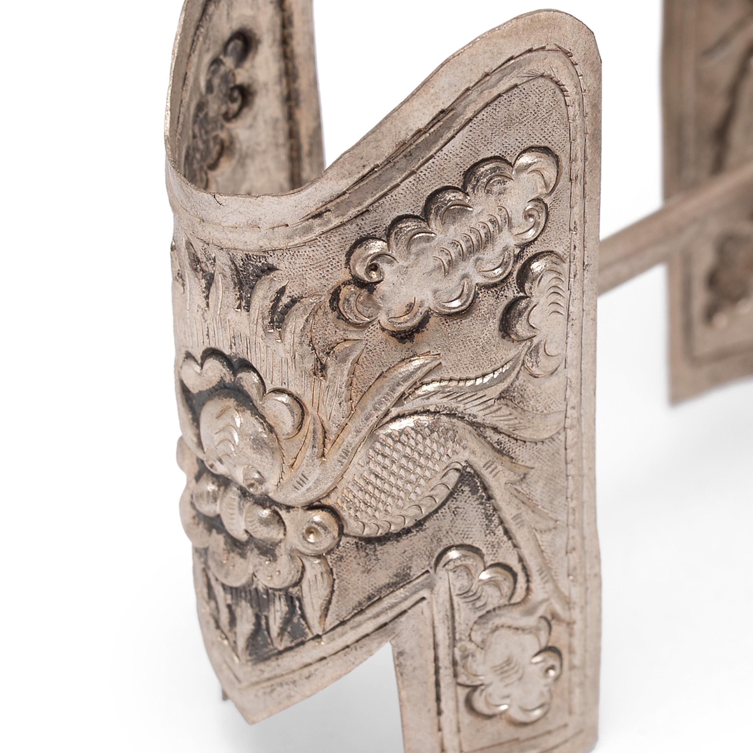 This unusual piece of silver hardware is wonderfully patterned with intricate Tibetan repoussé decoration. Comprised of two thin silver plates linked by a straight rod, the metal fitting is decorated on each side with a fearsome dragon, his feet in