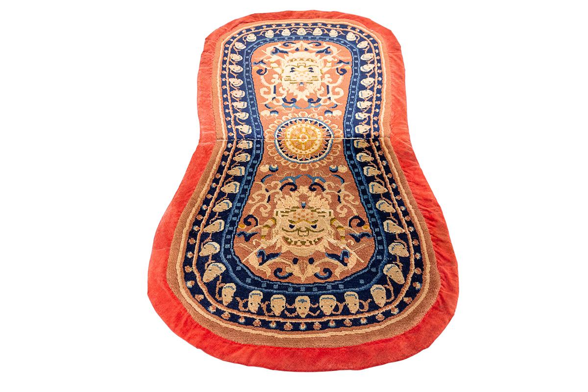 Dieser einzigartige tibetische Teppich mit Drachenmotiv misst 133 × 62 cm und zeichnet sich sowohl durch seinen Symbolreichtum als auch durch seine unverwechselbare Form aus. Die sanduhr- oder sattelförmige Form diente wahrscheinlich einem