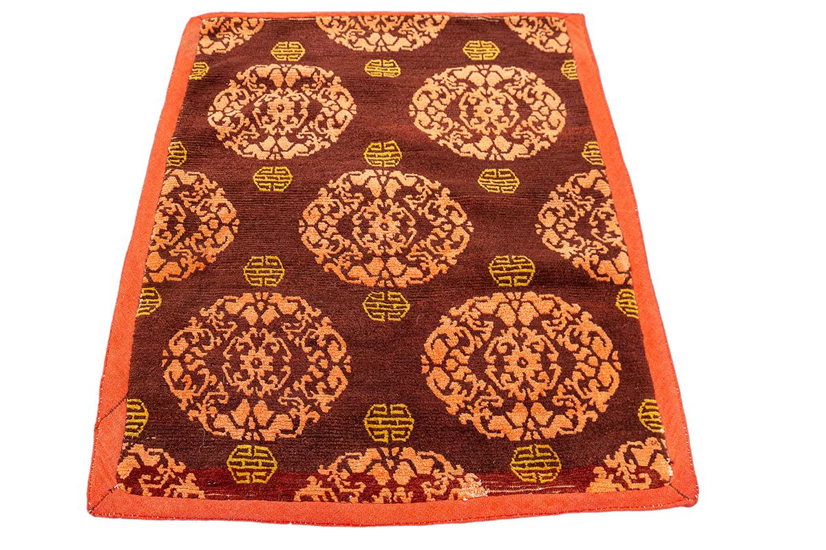 Questo tappeto tibetano finemente tessuto, che misura 64 × 80 cm, è un esempio compatto ed elegante di un tradizionale sedile da meditazione (dzong o khaden), utilizzato in ambienti monastici o domestici buddisti durante la preghiera, la meditazione