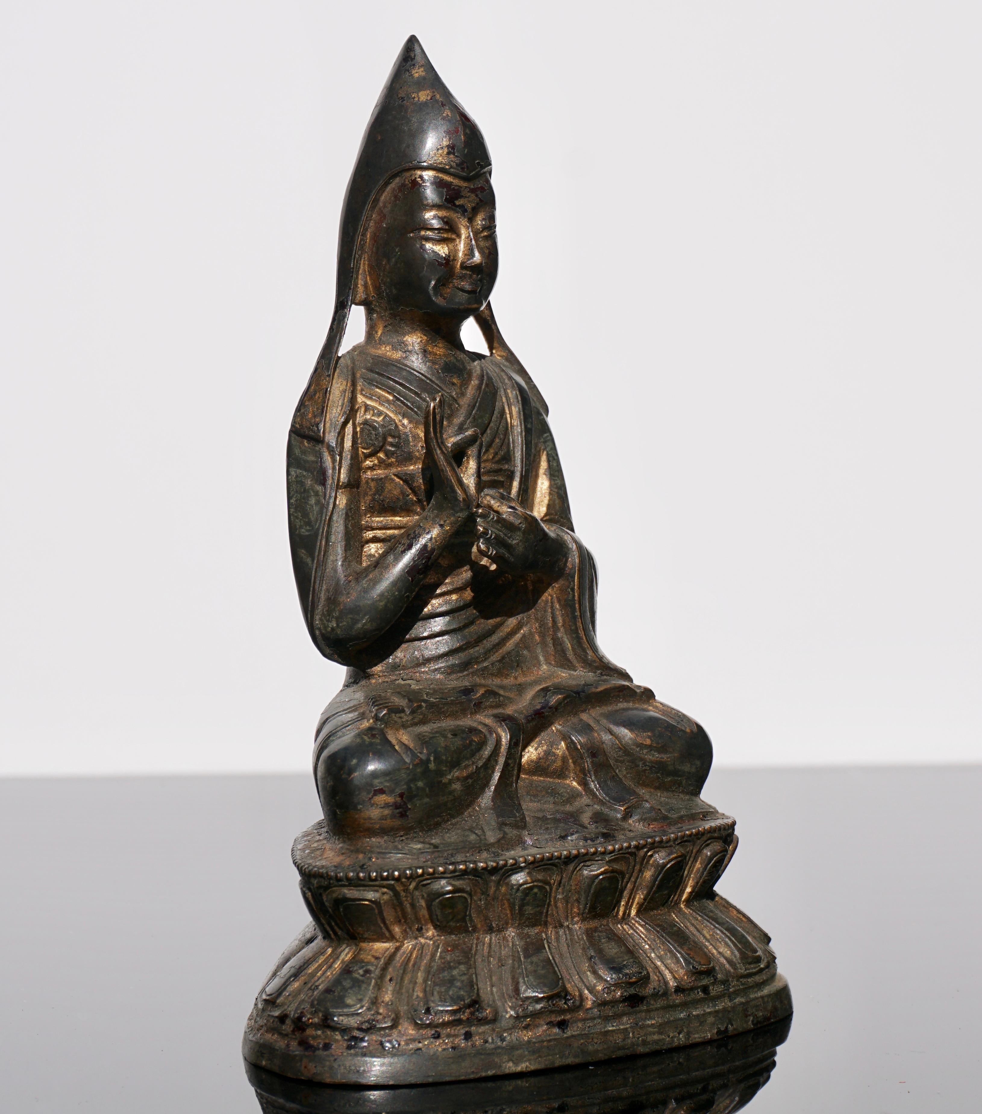 A gilt bronze figure of Tsong Khapa
Tibeto-Chinese, 18th-19th century
Seated on a double-lotus throne with hands in dharmachakra mudra, each holding the stem of a lotus, wearing a draping robe. His face with a benign expression, the lappets of his
