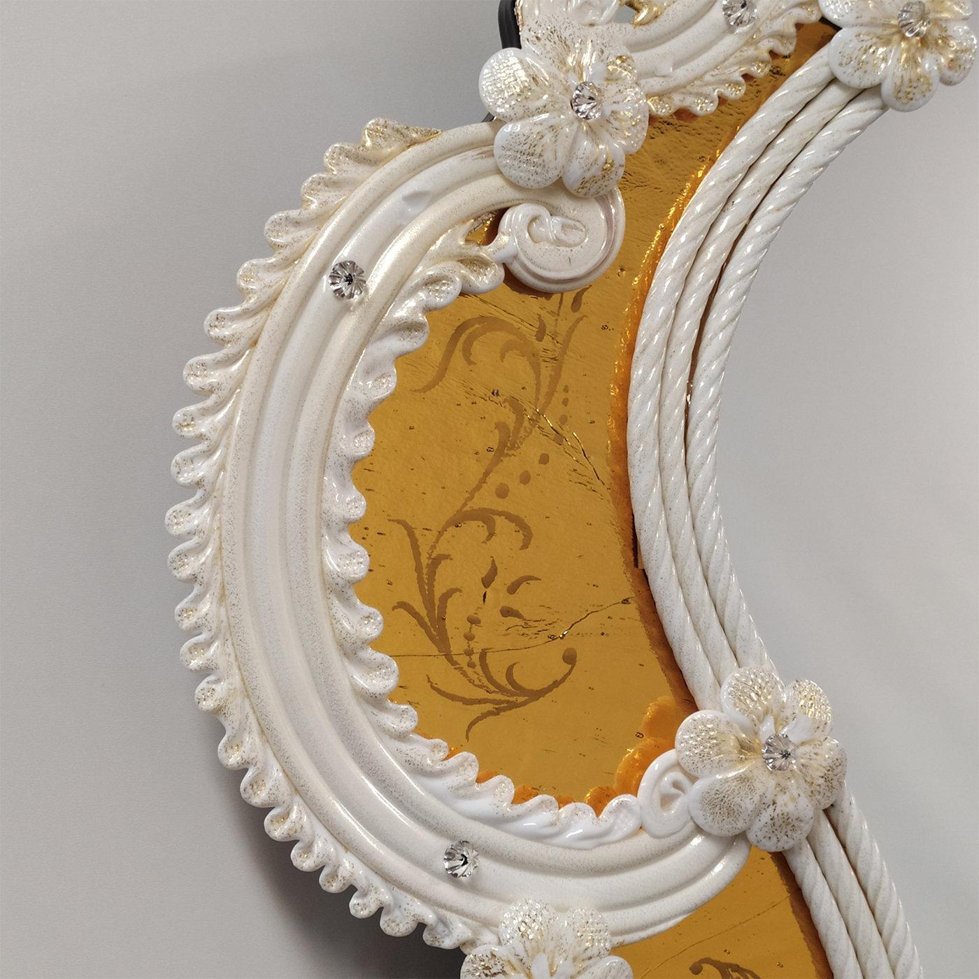 A gorgeous design of unparalleled elegance, this wall mirror sublimely reproduces the refined figure of an ancient Venetian style mirror, interpreted in a modern key with a new and brilliant choice of colors. Engraved by hand on an amber mirror, it