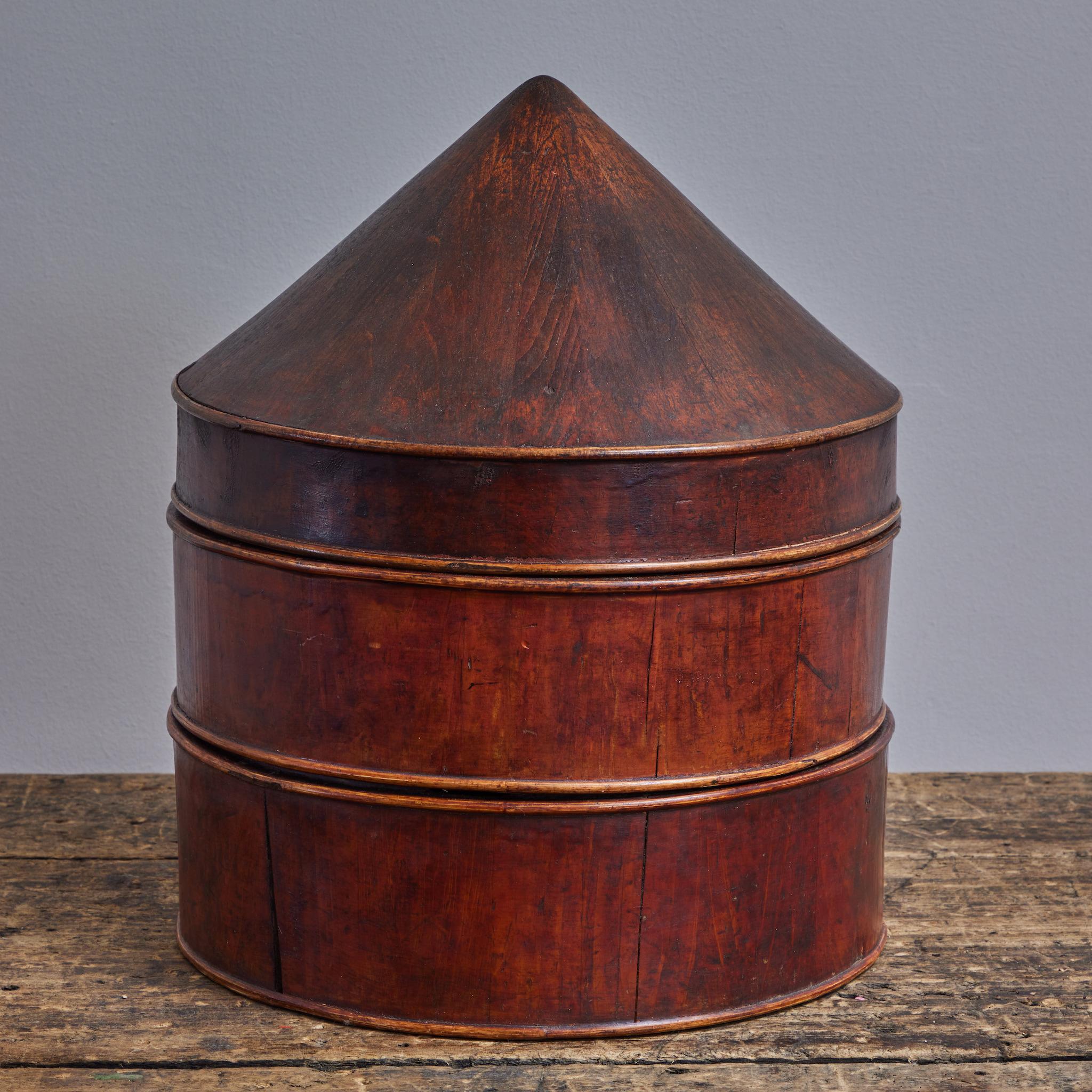 Chinese turn-of-the-century wooden hat box, with three tiered compartments. The conical lid gives the piece a sculptural quality, and is warmed by its bright and ruddy patina. A lovely and unique addition to any shelf or tabletop. 
