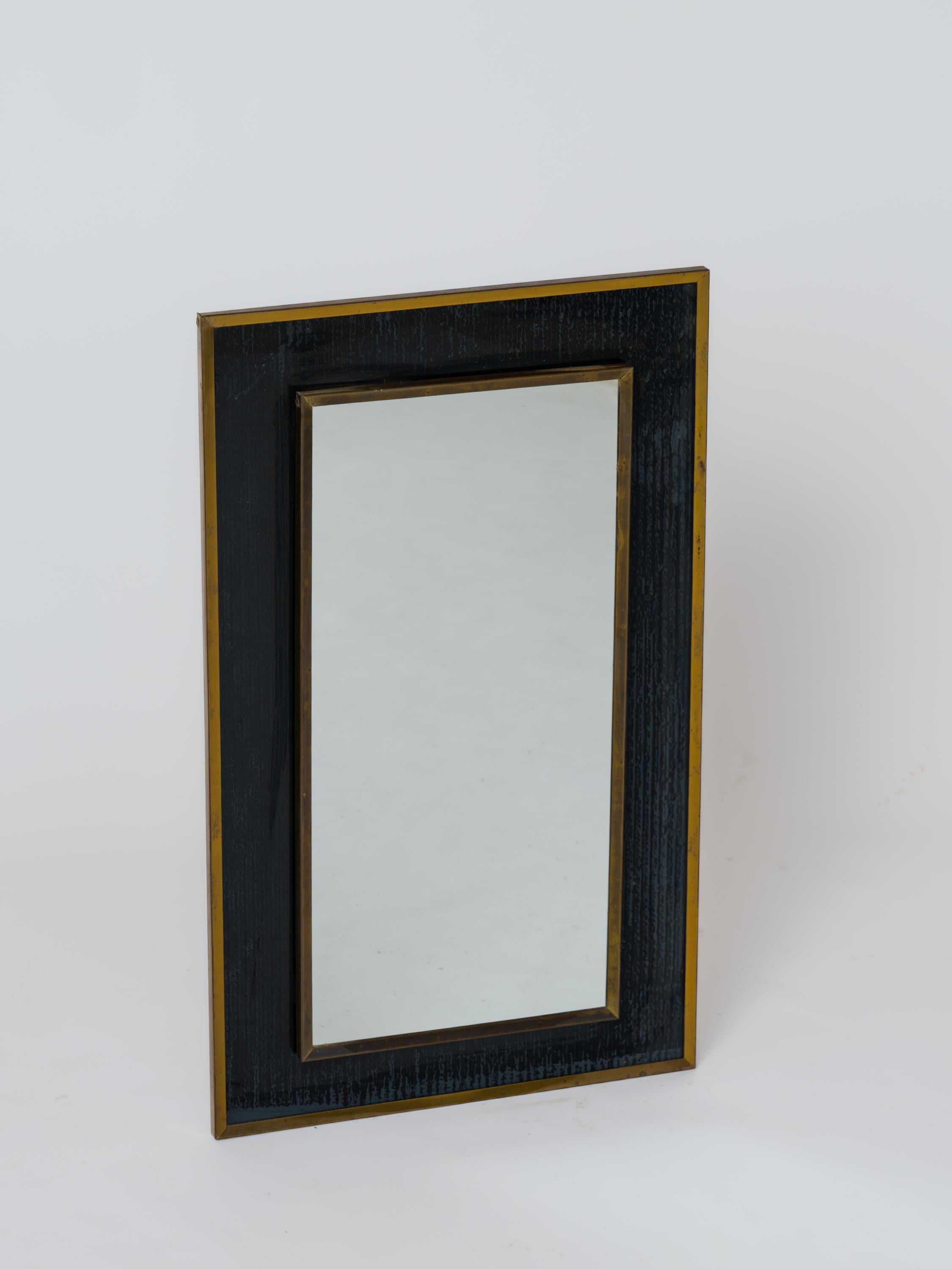 Piccolo specchio degli anni '70 in vetro verniciato a rovescio color nero petrolio, su cui poggia una sporgenza a specchio incorniciata da un bordo in ottone patinato.
Anche il pannello principale ha la stessa cornice. Sul retro è presente una