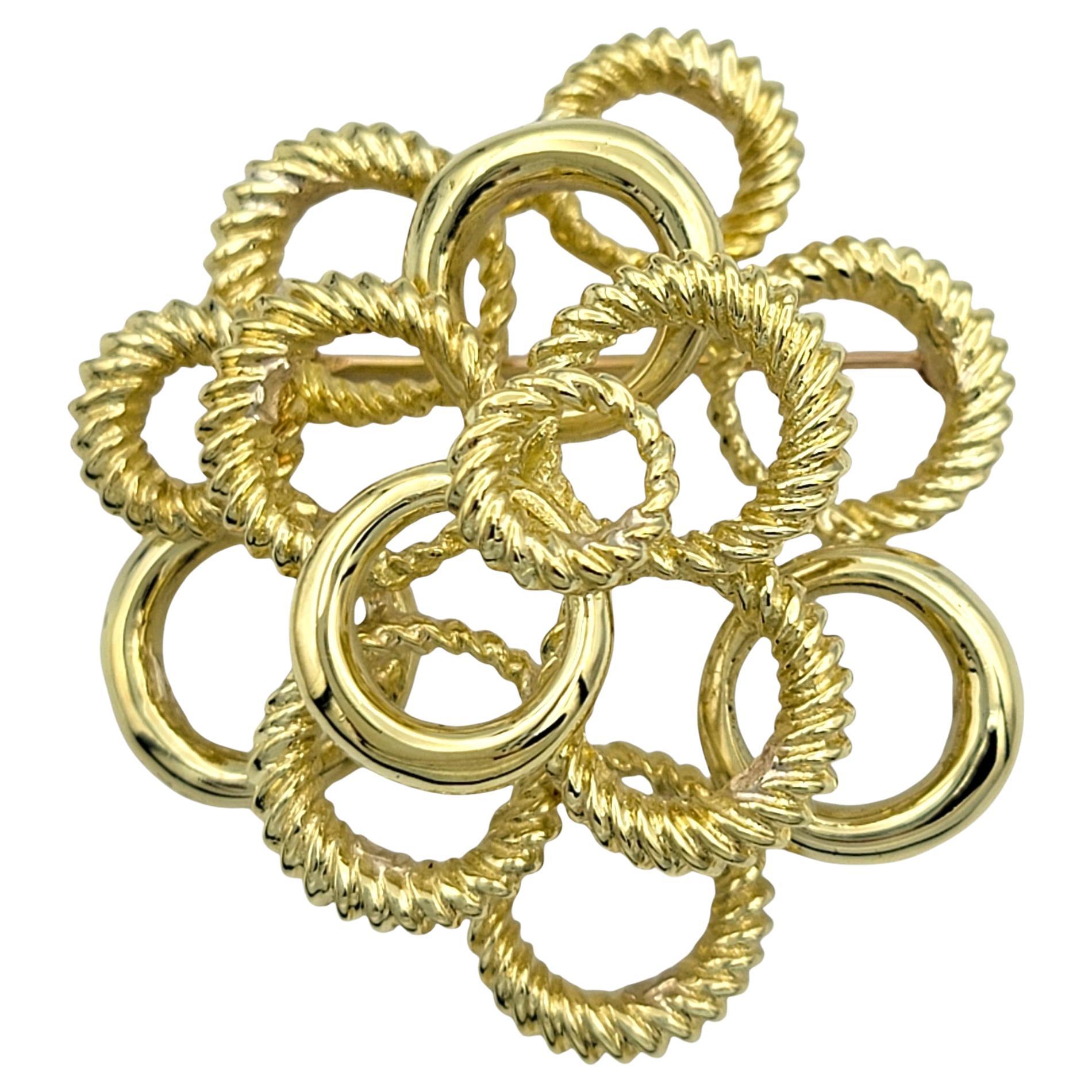 Irradia un toque de arte y sofisticación con este impresionante broche de oro amarillo de 18 quilates, una pieza única que celebra tanto la textura como la forma. Este broche presenta un fascinante conjunto de círculos dorados, ingeniosamente