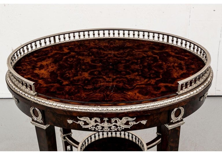 Constructed with a fine dark Burl wood veneer in a high polish. Oval in shape with polished silver tone mounts. The top with a 3/4 gallery, the frieze set with neoclassical mounts with hippocamps flanking urns and wreaths above the legs, Raised on