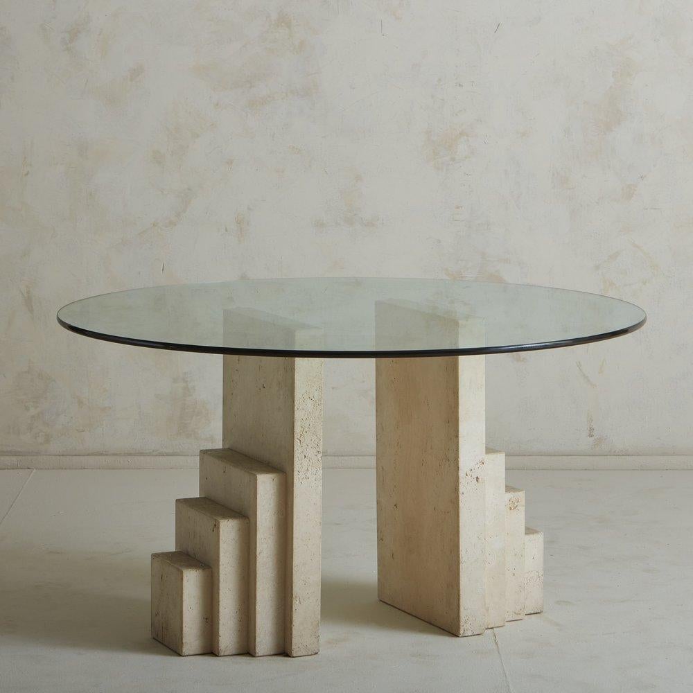 A 1970s Italian dining table featuring two tiered travertine bases with beautiful, natural movement in the stone. It has a circular glass tabletop with a bullnose edge. Unmarked. Sourced from a Villa in Italy, 1970s. 

DIMENSIONS: 51.75