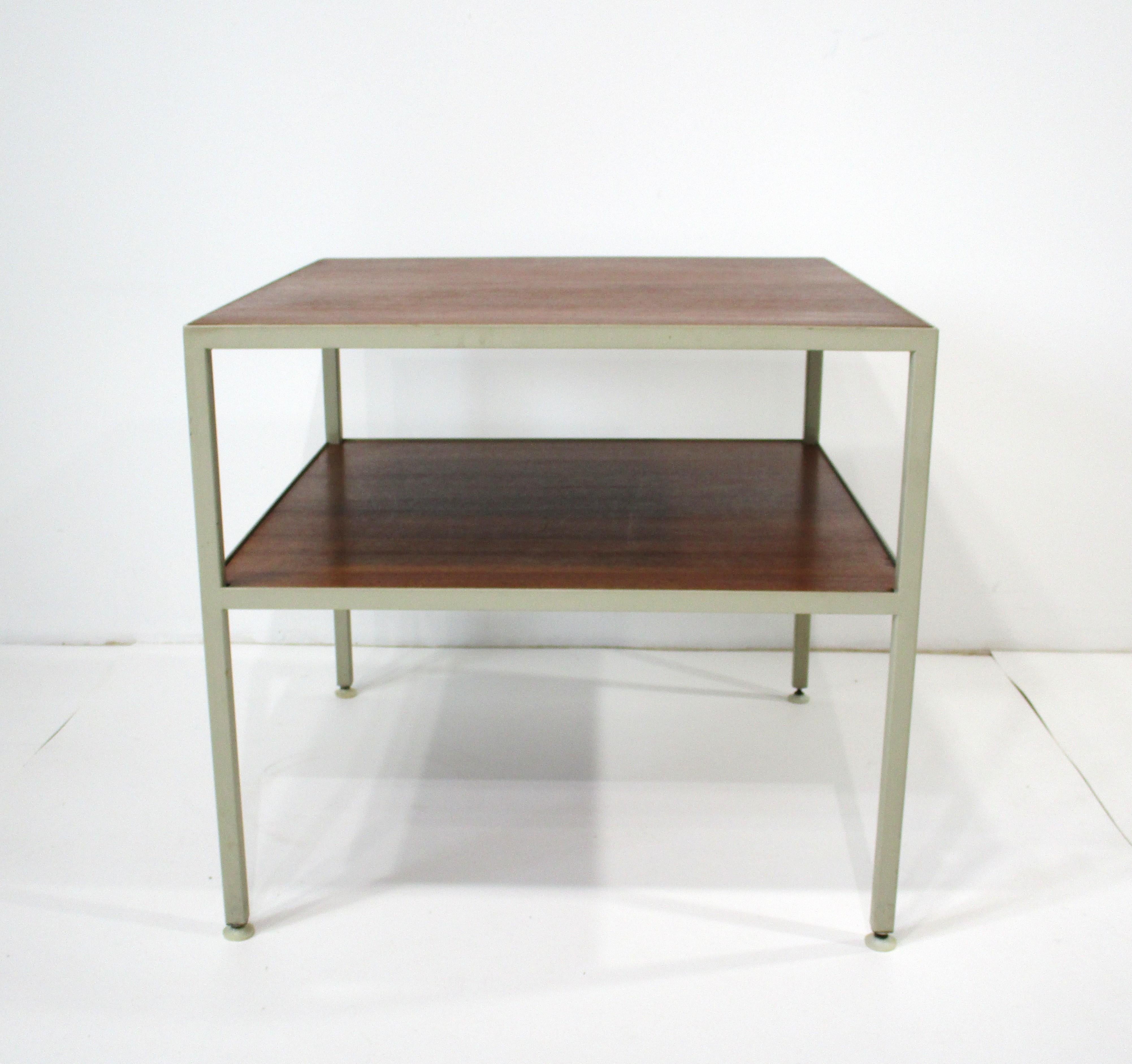 A two tiered walnut topped end or side table with a cream steel boxed frame and having foot pads to protect your floors . Very well crafted in the manner of George Nelson's steel frame furniture , manufactured by Janet Rosenblum and designed by
