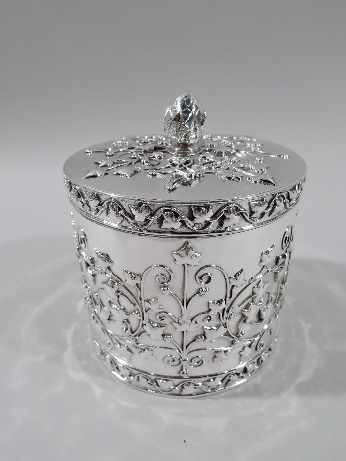 Aesthetic Revival sterling silver tea caddy. Retailed by Tiffany & Co. in New York. Drum form and flat cover with acorn finial. Applied tracery-style ornament with stylized vegetation and scrollwork between wavy leafing-branch borders. Perfect for a