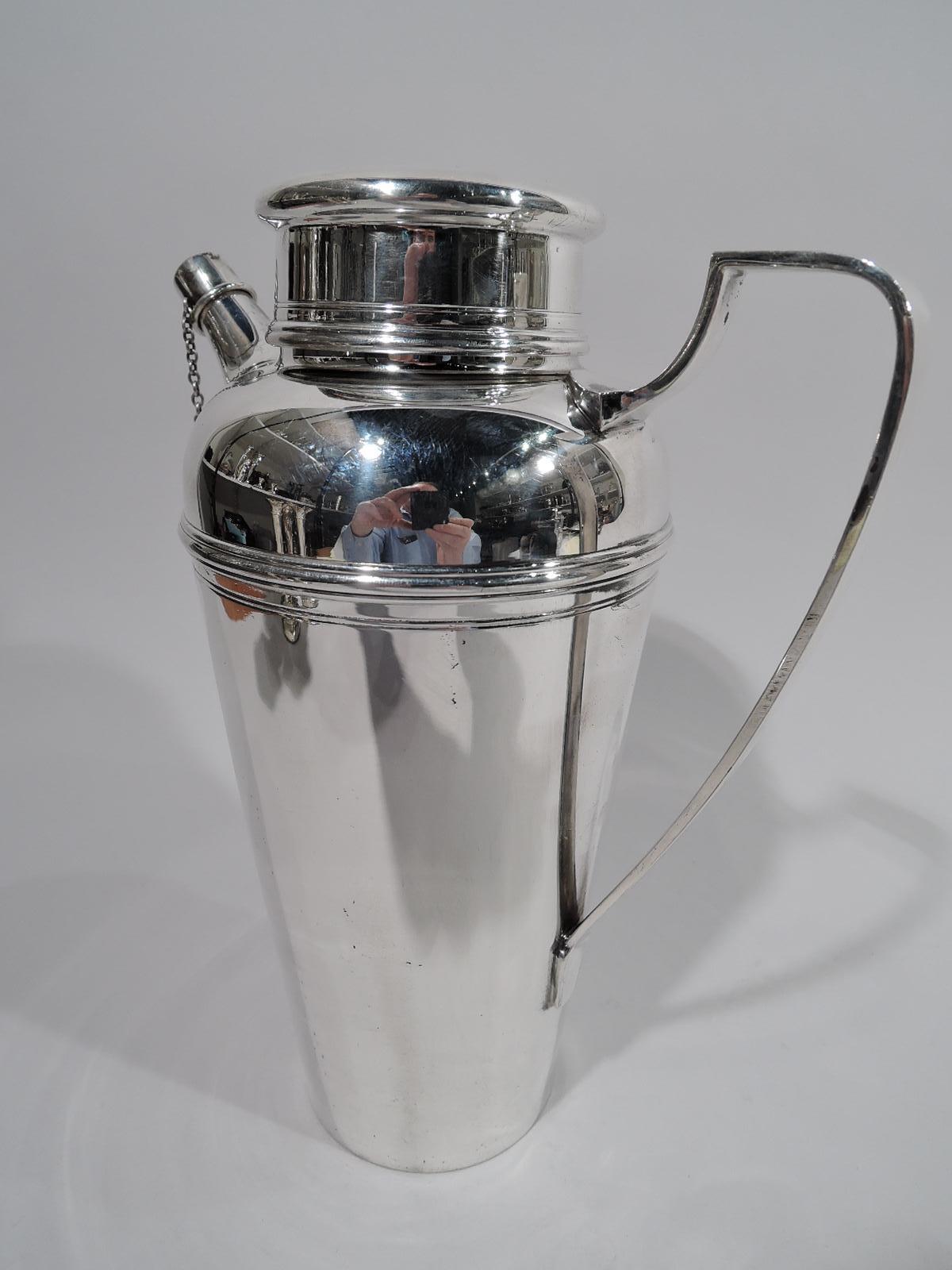 Art Deco sterling silver cocktail shaker. Made by Tiffany & Co. in New York. Straight and tapering bowl with curved shoulder, high scrolled bracket handle, short neck with overhanging flat-topped cover, and stubby, tapering spout with chained cap.