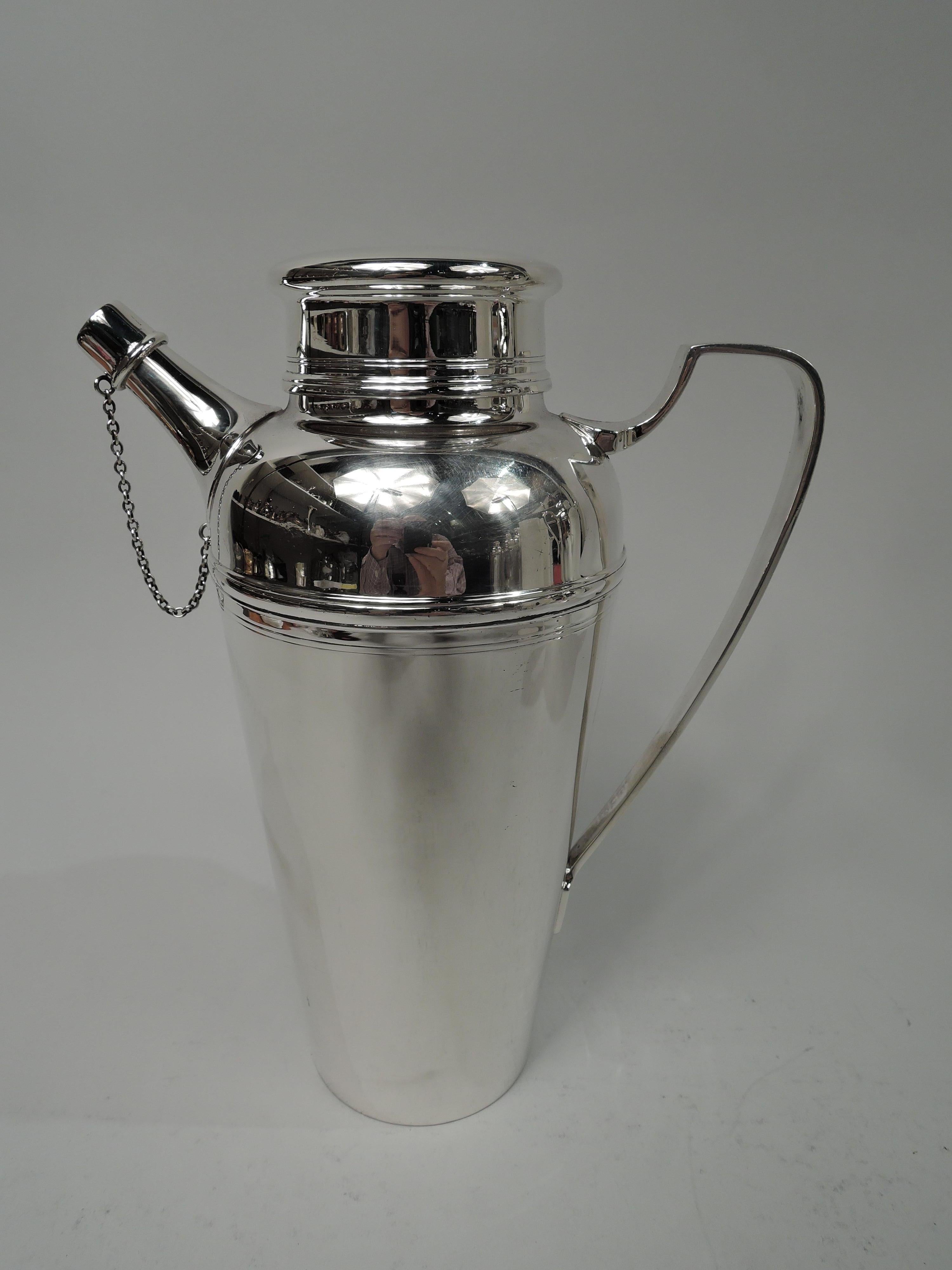 Art Deco sterling silver cocktail shaker. Made by Tiffany & Co. in New York, ca 1925. Straight and tapering bowl with curved shoulder, high bracket handle, short neck with overhanging flat-topped cover, and stubby, tapering spout with chained cap.