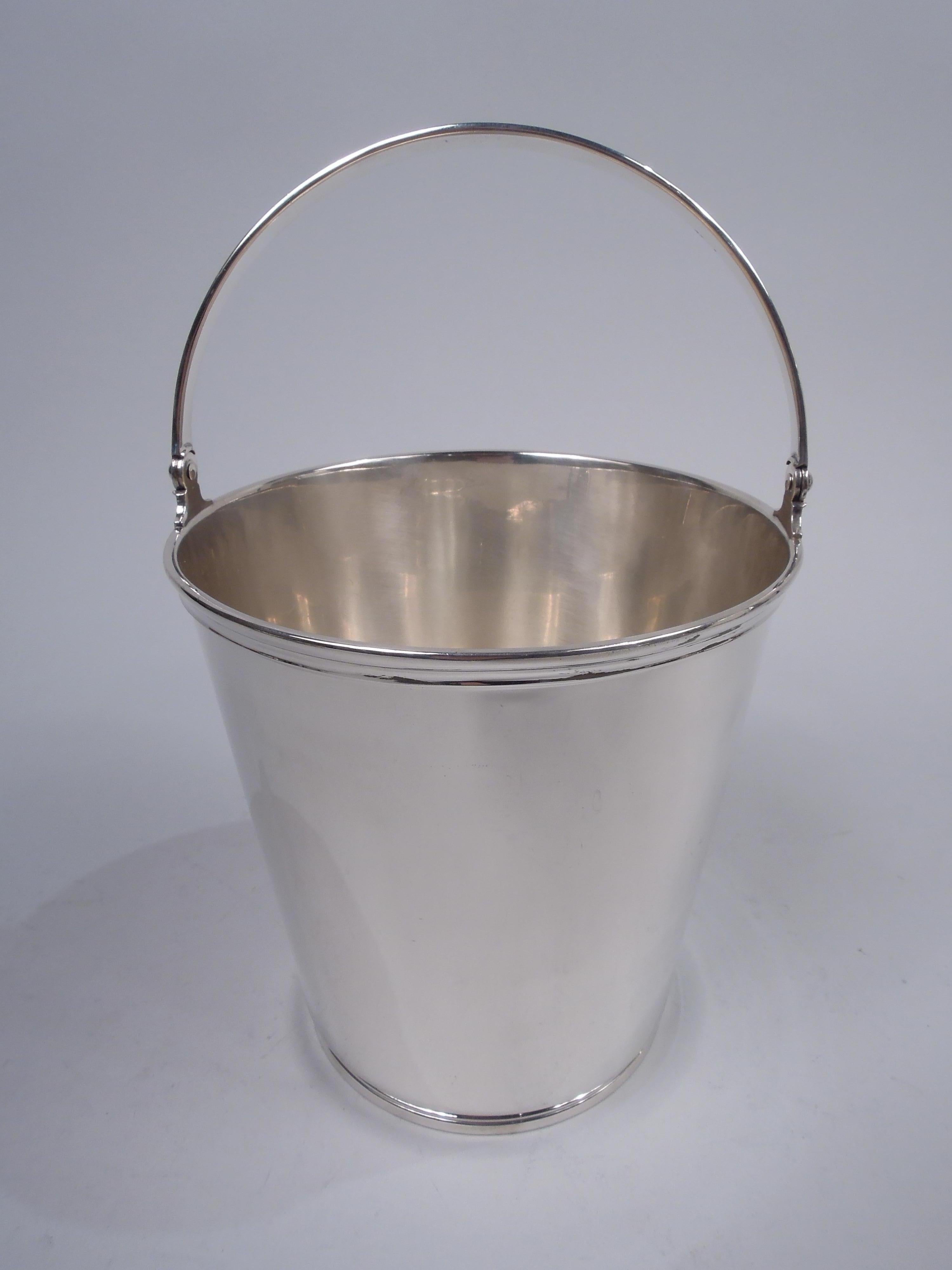 Art Deco sterling silver ice bucket. Made by Tiffany & Co. in New York, ca 1927. Straight and tapering sides with molded rim and foot ring; c-scroll swing tapering swing handle with incised linear borders. A smart and practical prohibition-era