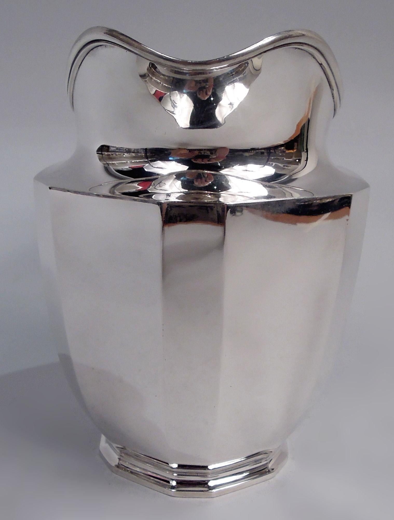 Pichet à eau Art déco en argent massif. Fabriqué par Tiffany & Co. à New York, ca. 1914. Corps incurvé, pied en escalier, bouche en forme de casque et poignée en forme d'étrier. Alternance de facettes larges et étroites sur le corps et le pied.