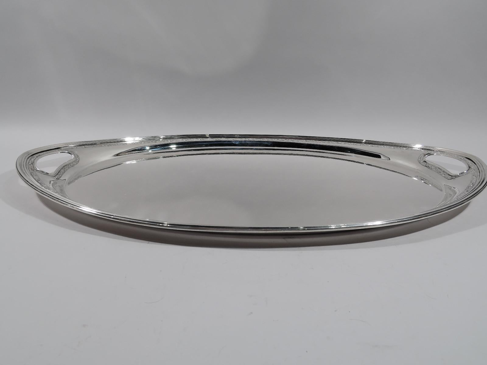 Large and heavy sterling silver tea tray. Made by Tiffany & Co. in New York, circa 1911. Oval well with tapering shoulder and reeded rim. Pointed ends with cutout oval handles. Discreet scrollwork engraved between pointille borders. Fully marked