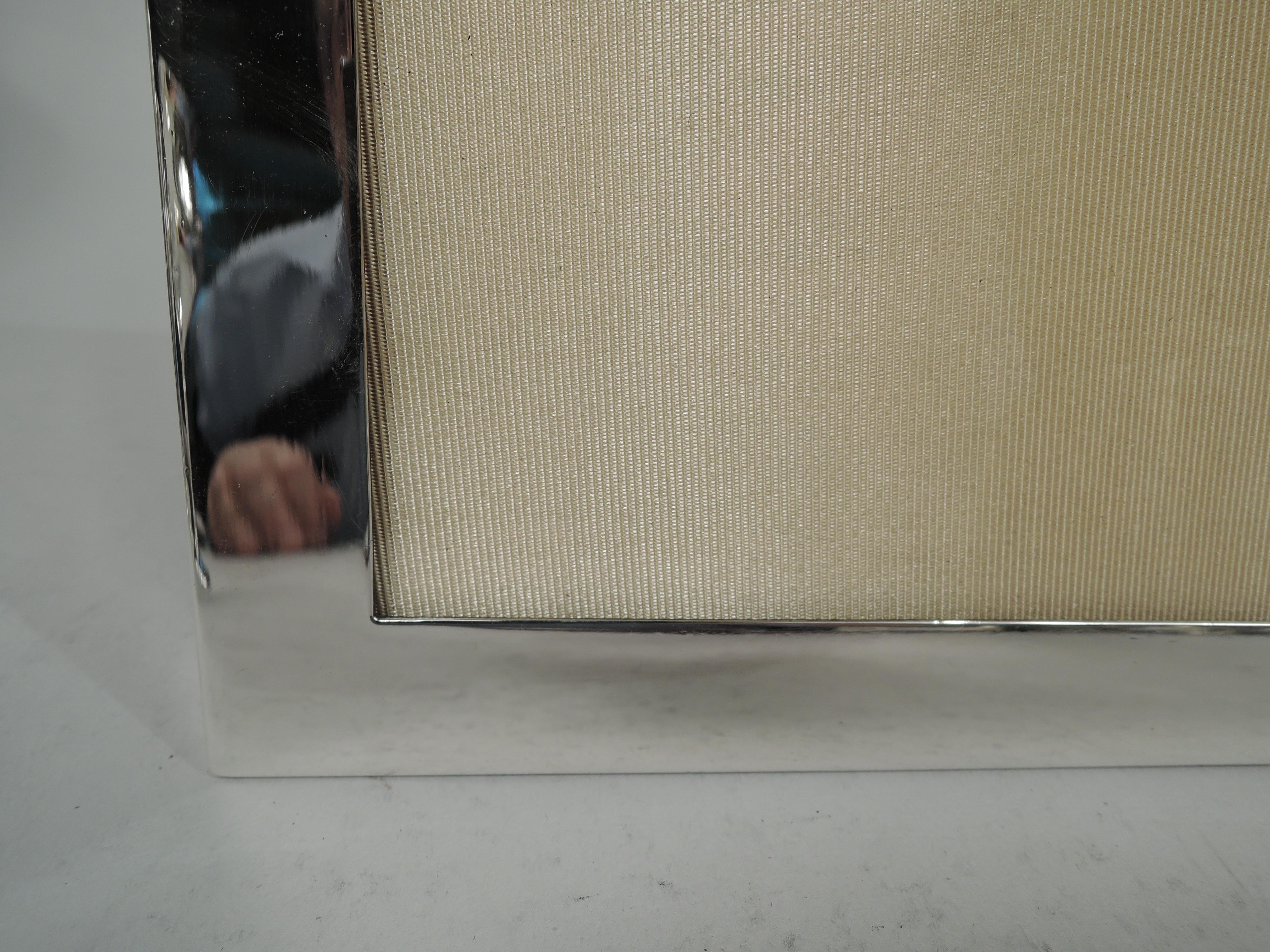 Moderner Edwardianischer Bilderrahmen aus Sterlingsilber. Hergestellt von Tiffany & Co. in New York, ca. 1910. Rechteckiges Fenster in gleicher schlichter und flacher Einfassung; unteres Geländer gekippt. Mit Glas, Seidenfutter, Samtrücken und