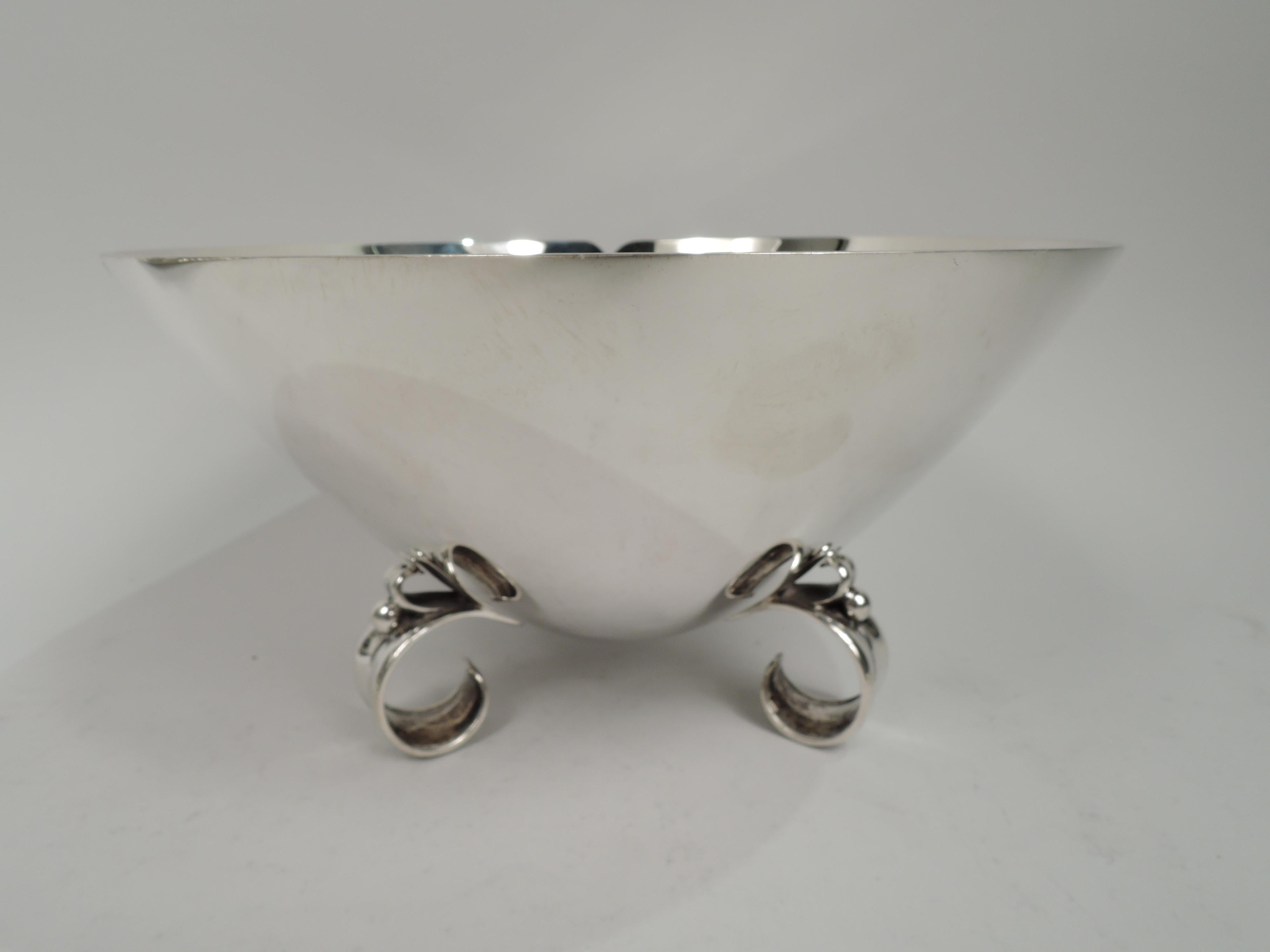 Midcentury Modern sterling silver bowl. Cone comprising 3 curved and incised panels with shallow petal rim. Tripod support comprising 3 concave c-scrolls with bead and scroll mount. The mount and its reflection form a heart. A clever illusory design