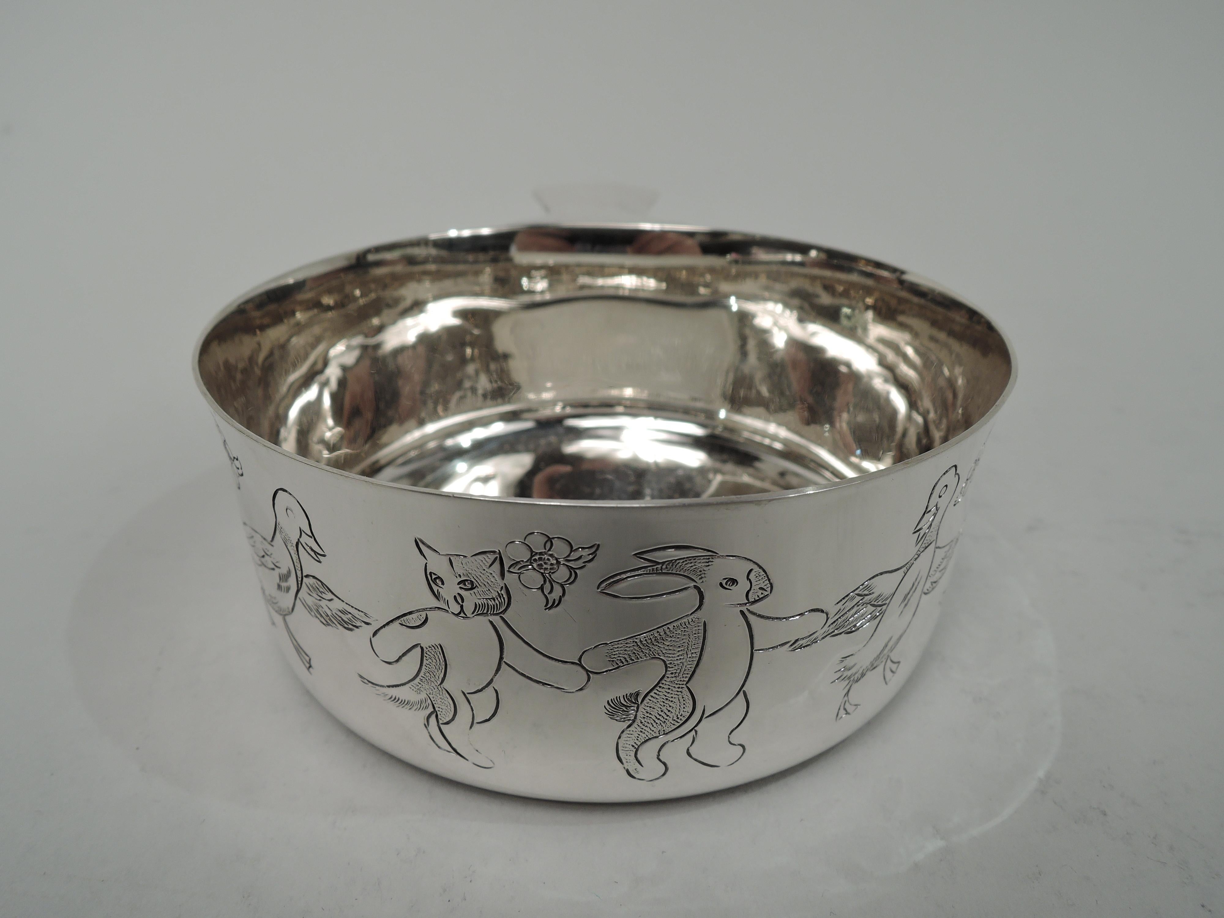 Mid-Century Modern sterling silver porringer. Made by Tiffany & Co. in New York. Round with straight sides, flared rim, and chamfered and tapering solid handle. Frieze with birds, bunnies, and kitties dancing paw in wing. Fully marked including